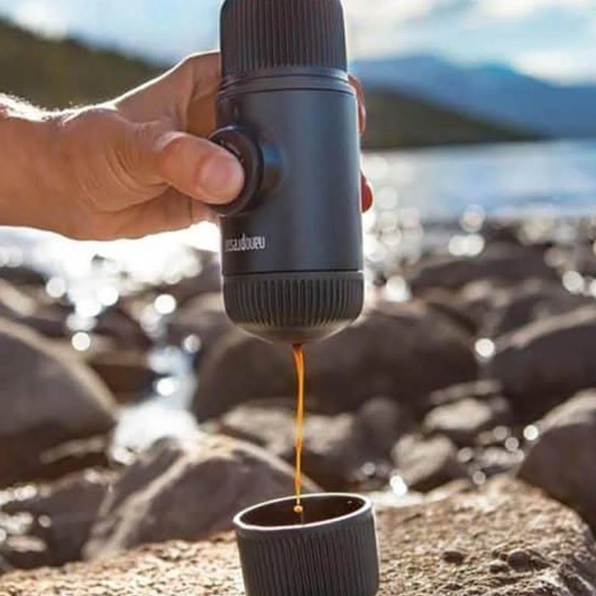 Die Hand einer Person, die mit einem tragbaren Espressomaschine Kaffee zubereitet.