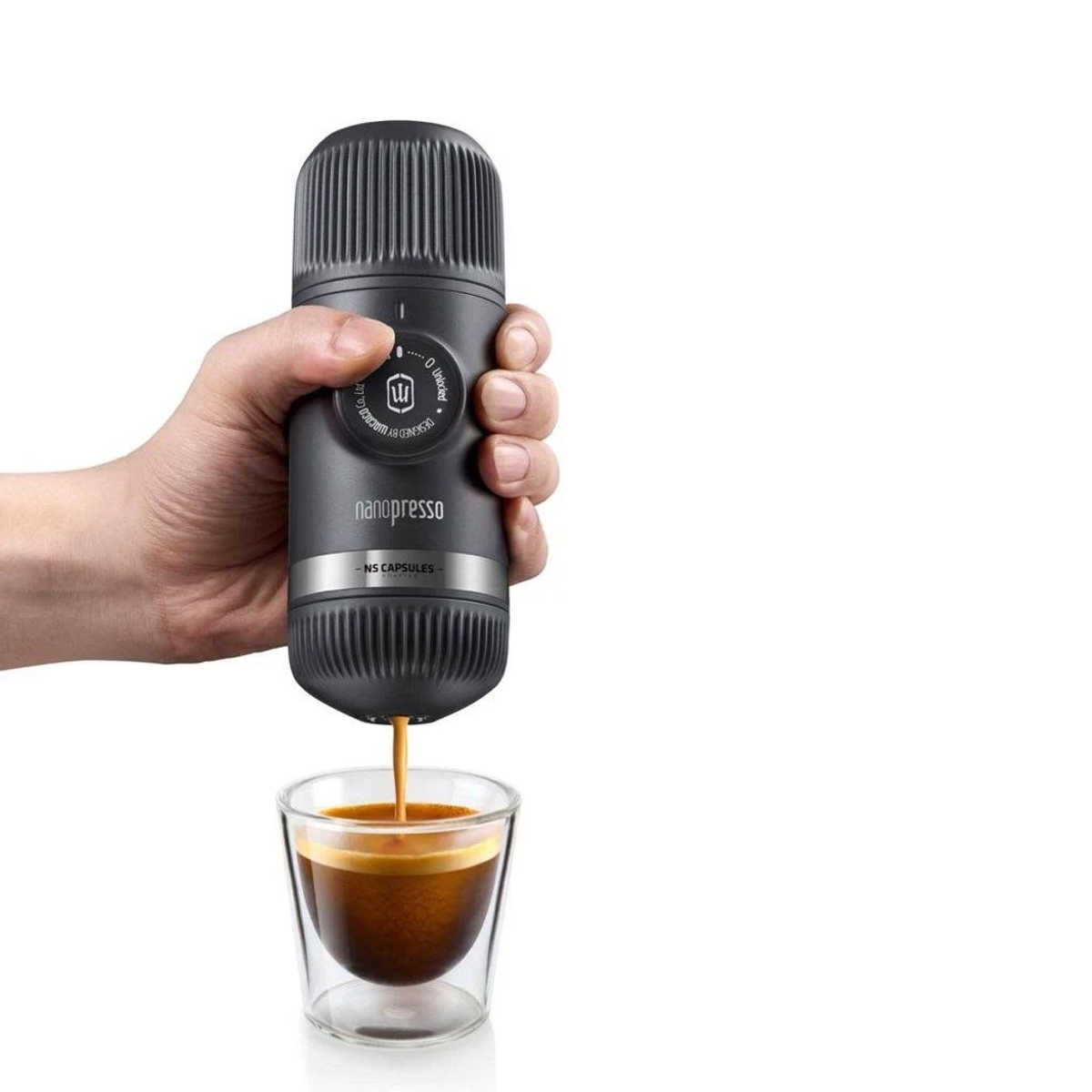 Eine Hand hält einen grauen Nanopresso-Kaffeezubereiter, der Espresso in ein Glas ausgibt, vor weißem Hintergrund.