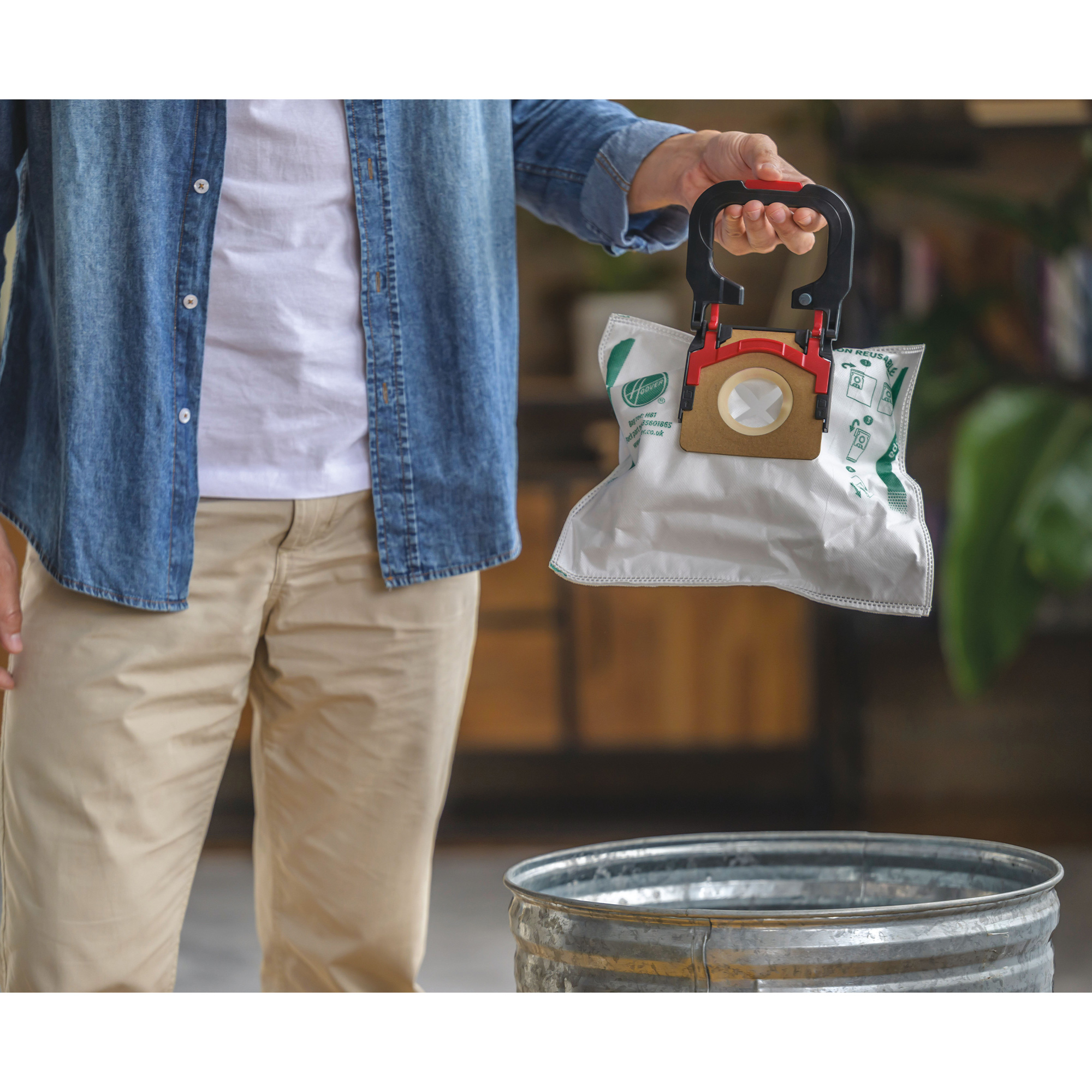 Osoba trzymająca worek do odkurzacza. W tle znajduje się kosz na śmieci.