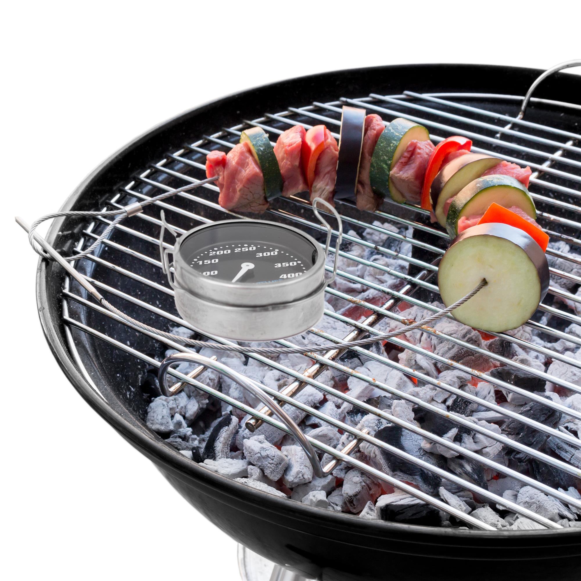 Ein Holzkohlegrill mit Thermometer und Spießen mit Fleisch und Gemüse. Holzkohle befindet sich am Boden.