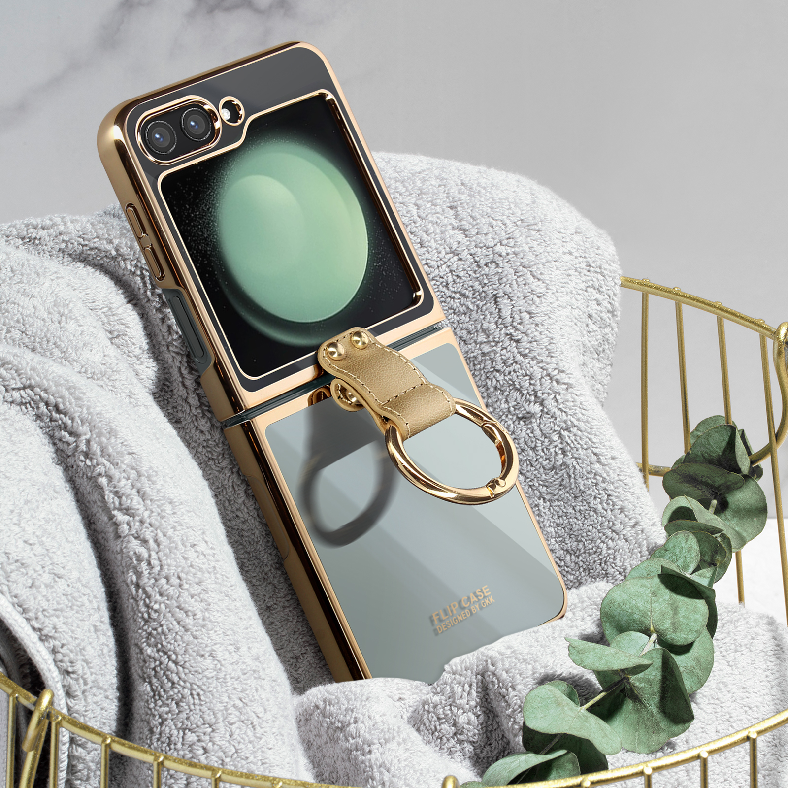 Custodia pieghevole per telefono con anello. Il telefono è su un asciugamano grigio in un cestino dorato. Foglia verde.