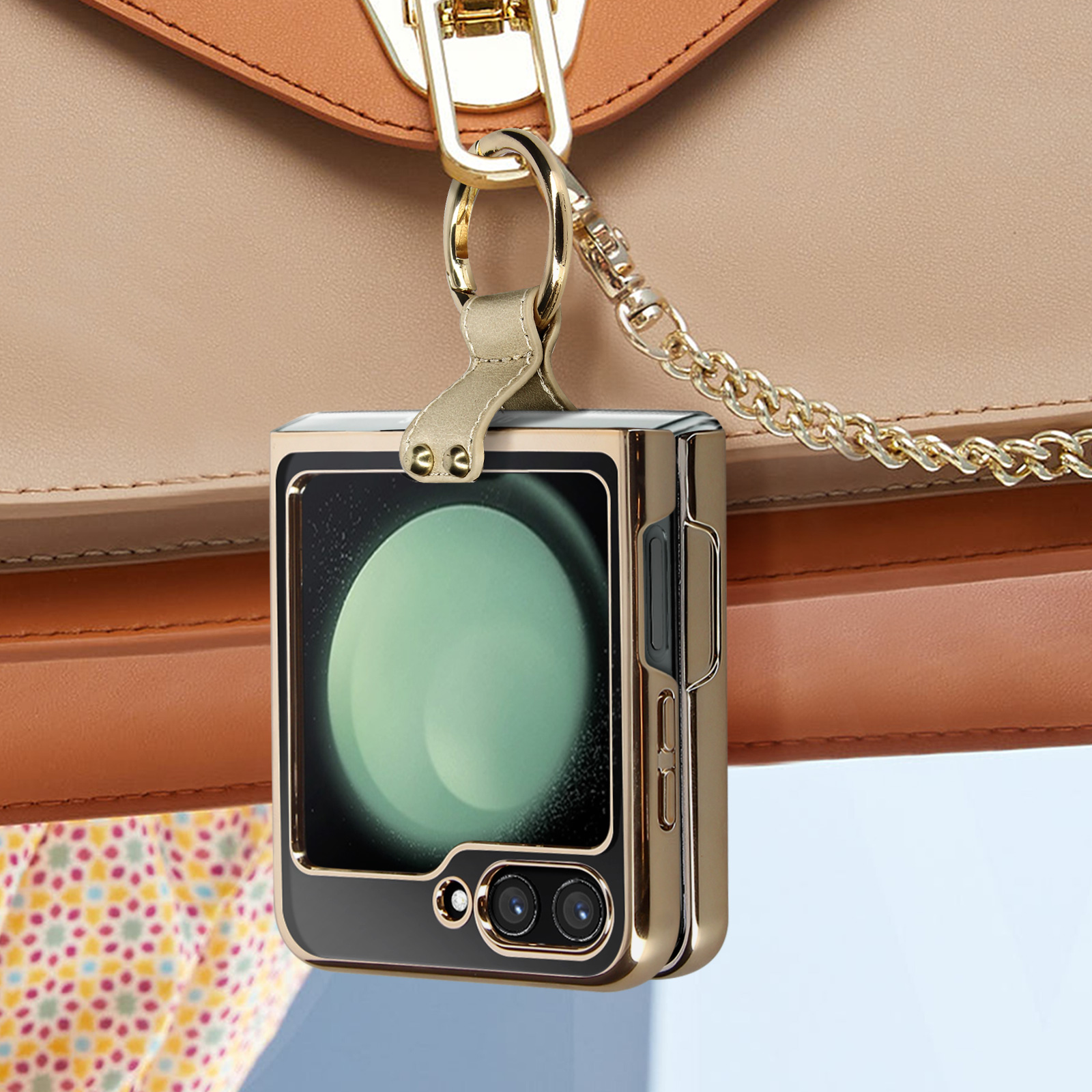 Una custodia dorata per telefono attaccata a una borsa beige con una tracolla a catena dorata, appesa.