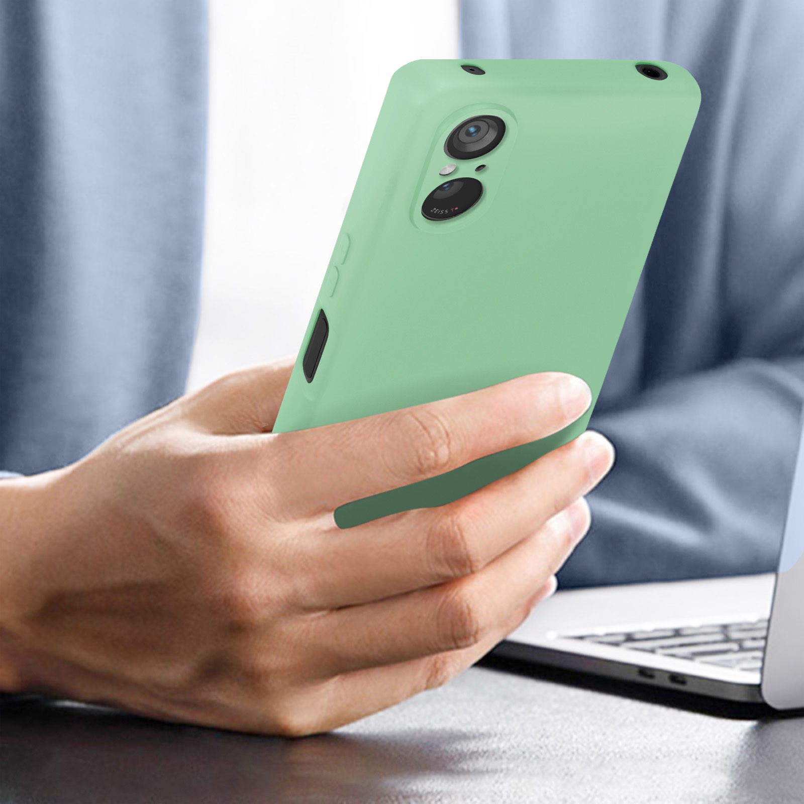 Una persona che tiene in mano un telefono verde chiaro. La fotocamera del telefono è visibile.
