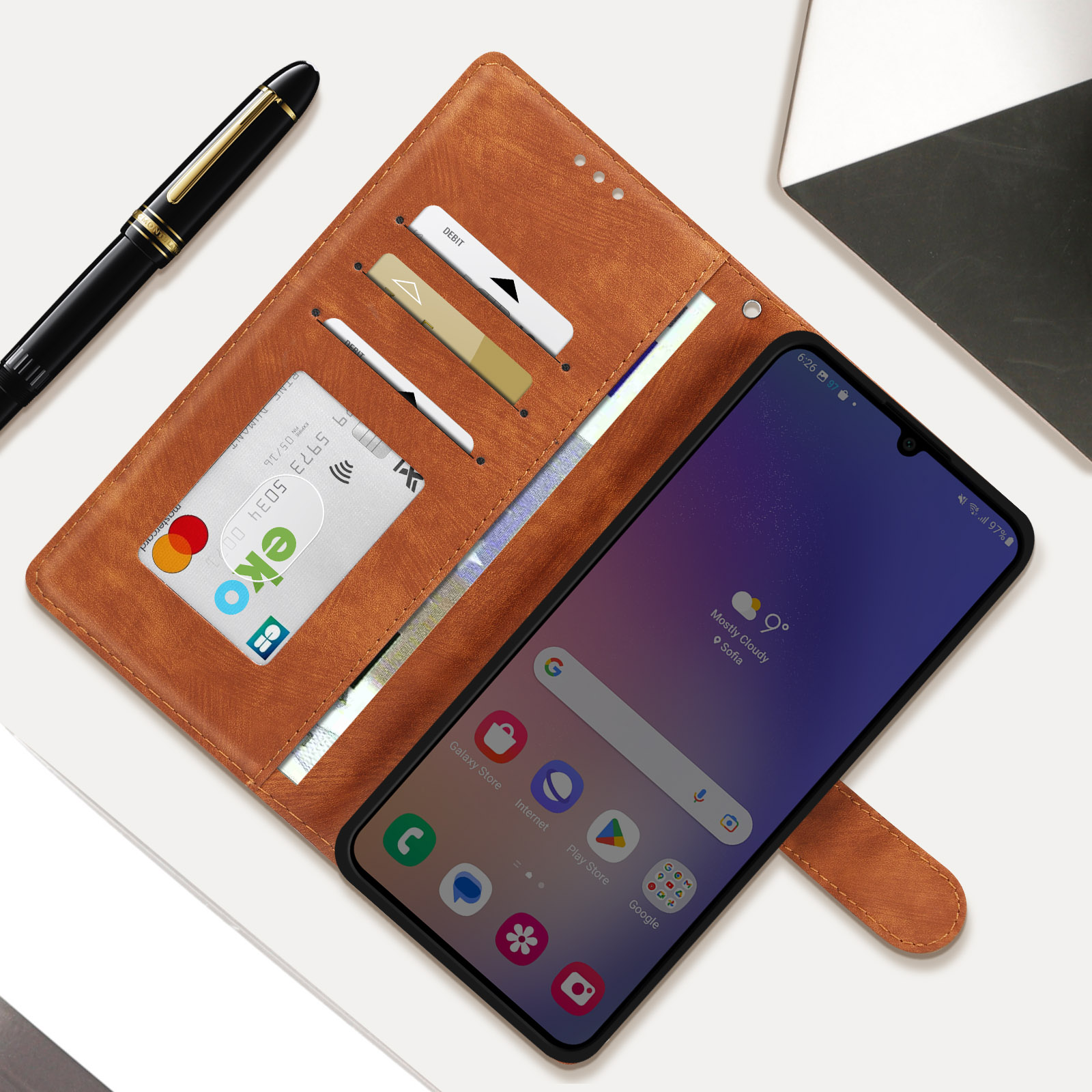 Custodia marrone aperta con telefono, carte e penna. Il telefono mostra l'app meteo.