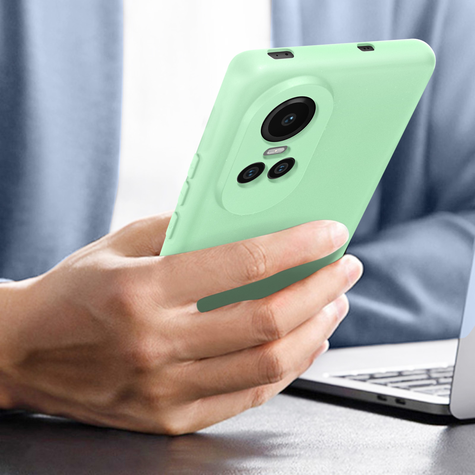 Custodia per telefono verde chiaro con sporgenza fotocamera, tenuta sopra un laptop.