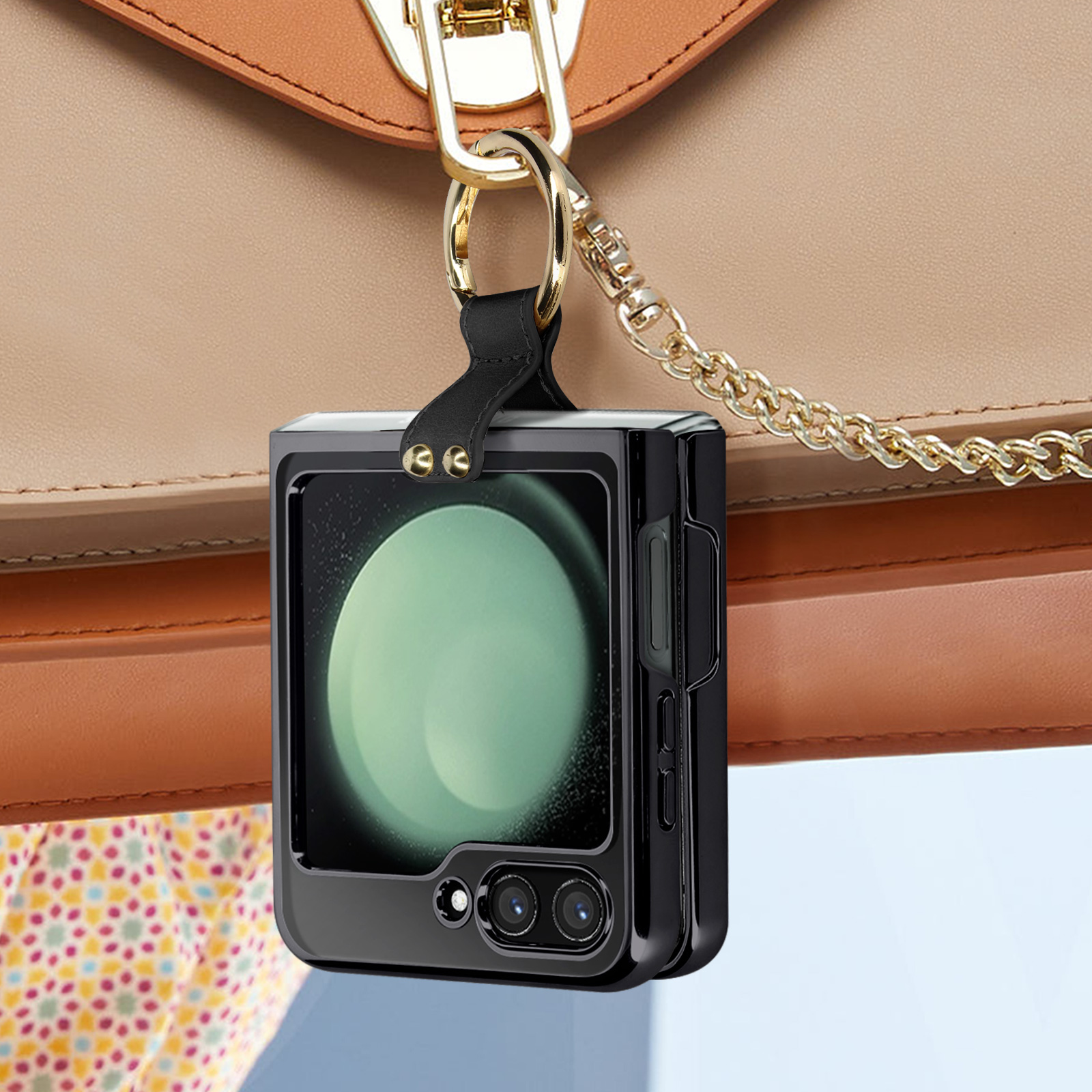 Schwarze Handyhülle hängt an einer beigen Handtasche. Sie hat eine goldene Kette und ein Telefon darin.