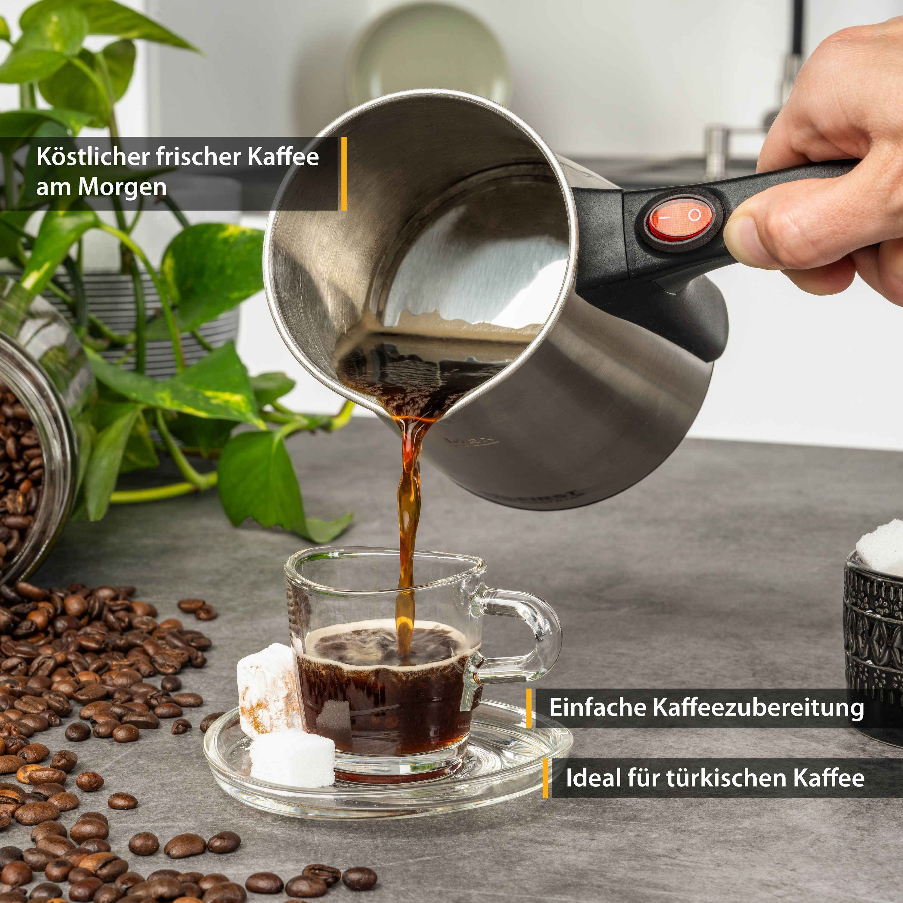 Kaffee wird in ein Glas gegossen. Der Topf hat einen roten Knopf. Kaffeebohnen und Zucker sind auf der Seite.
