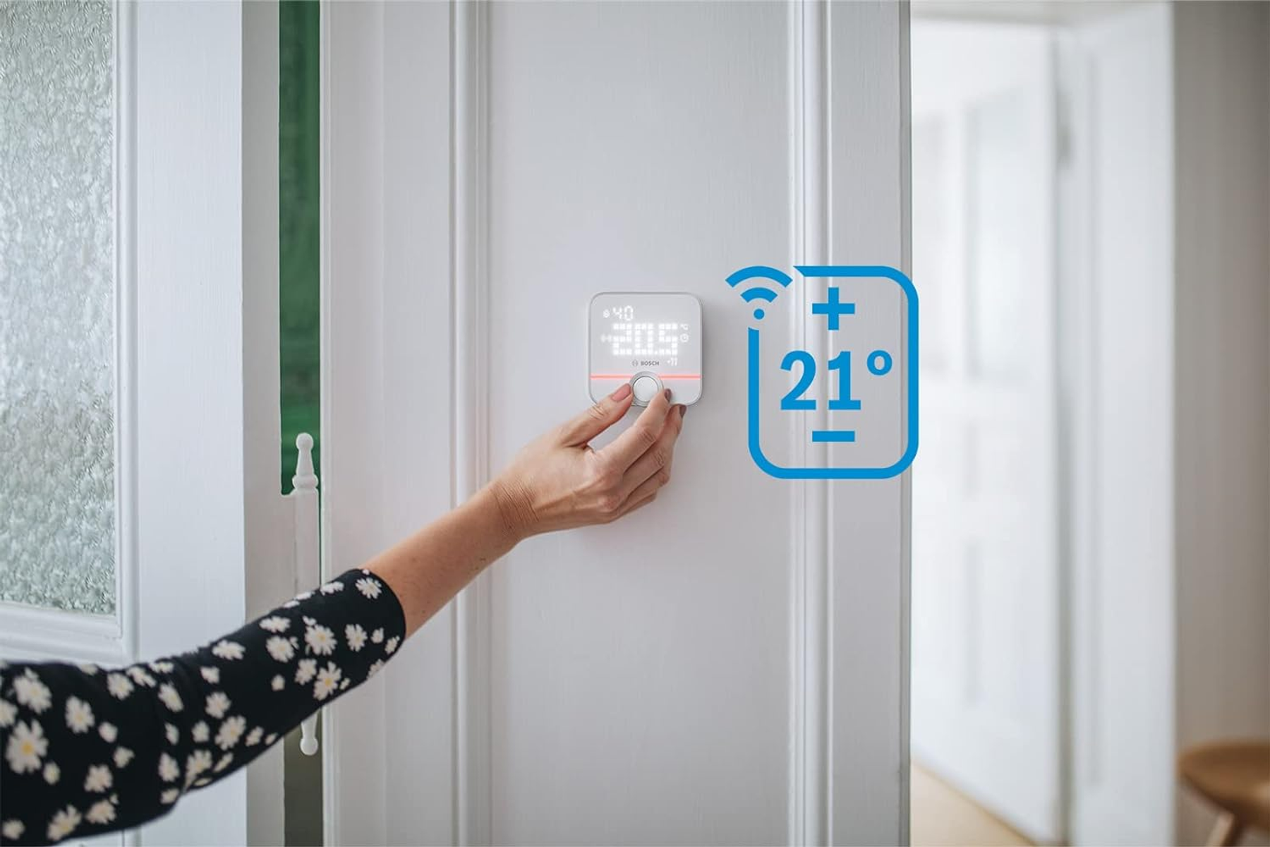 Hand einer Person, die einen intelligenten Thermostat an einer weißen Wand einstellt. Digitalanzeige zeigt Temperatur.