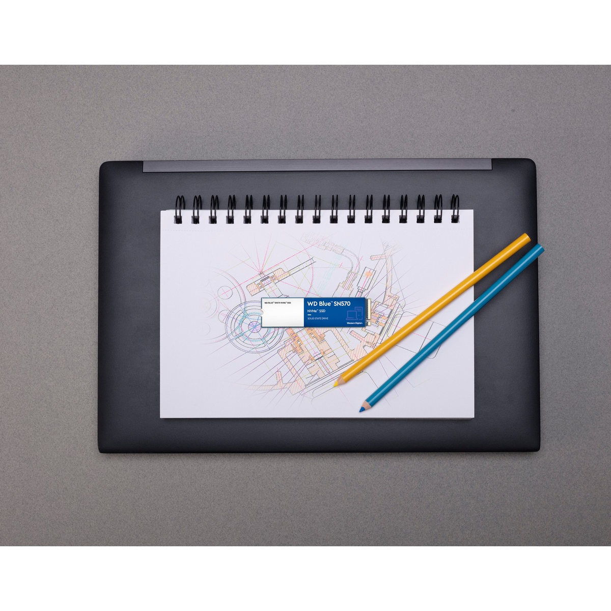 Notatnik ze szkicem, ołówkami i etykietą WD Blue SSD na ciemnej powierzchni.