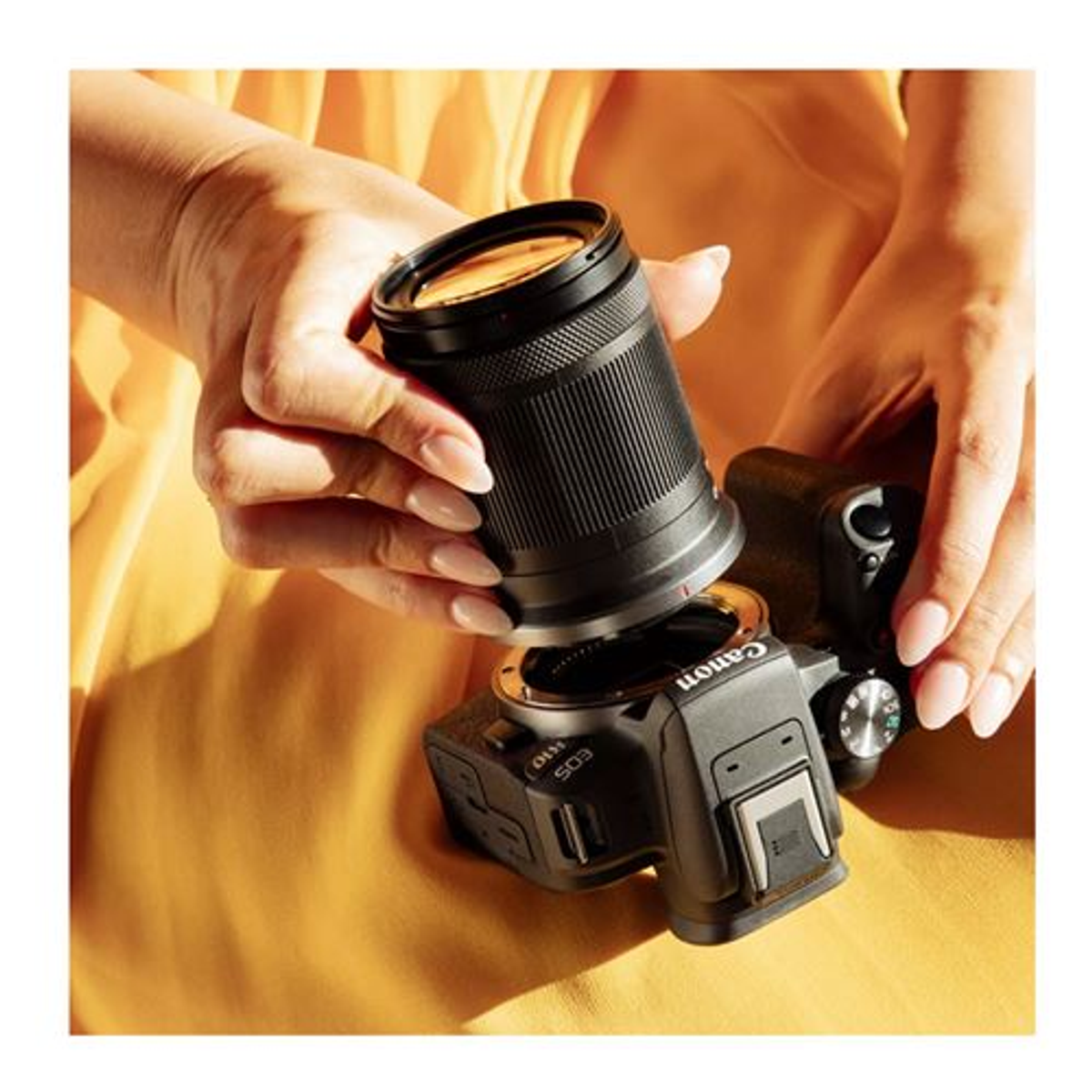 Osoba mocuje czarny obiektyw do czarnego aparatu Canon na żółtym tle.