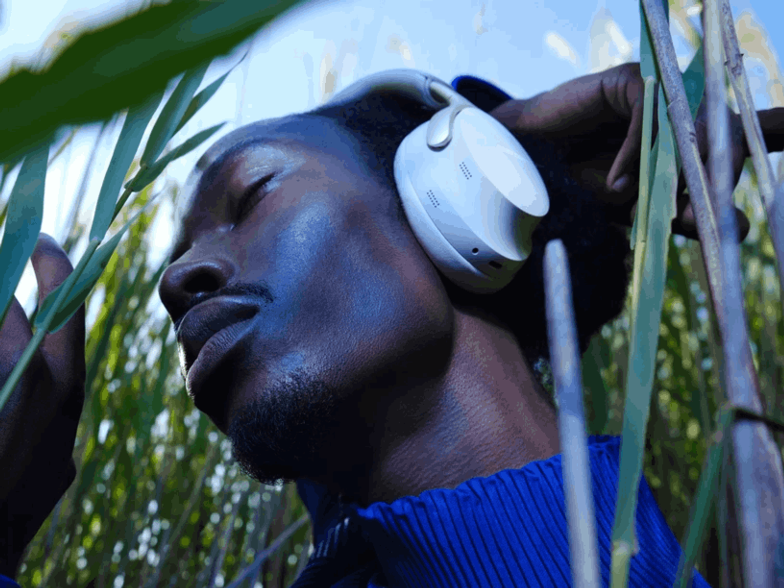 Mężczyzna w białych słuchawkach. Jest na polu wysokiej trawy, oczy zamknięte.