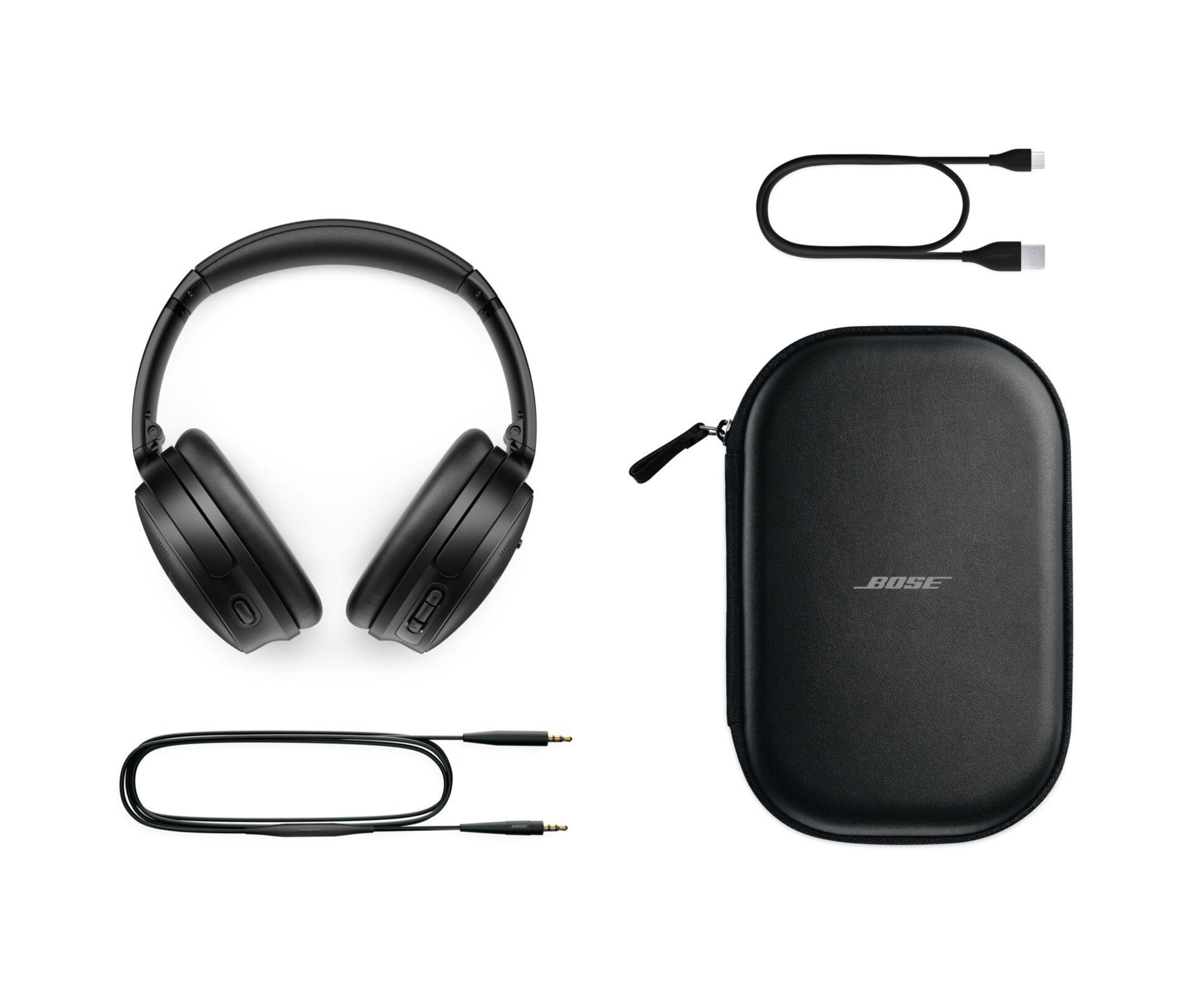 Auriculares, estuche y cables de carga negros sobre superficie blanca.