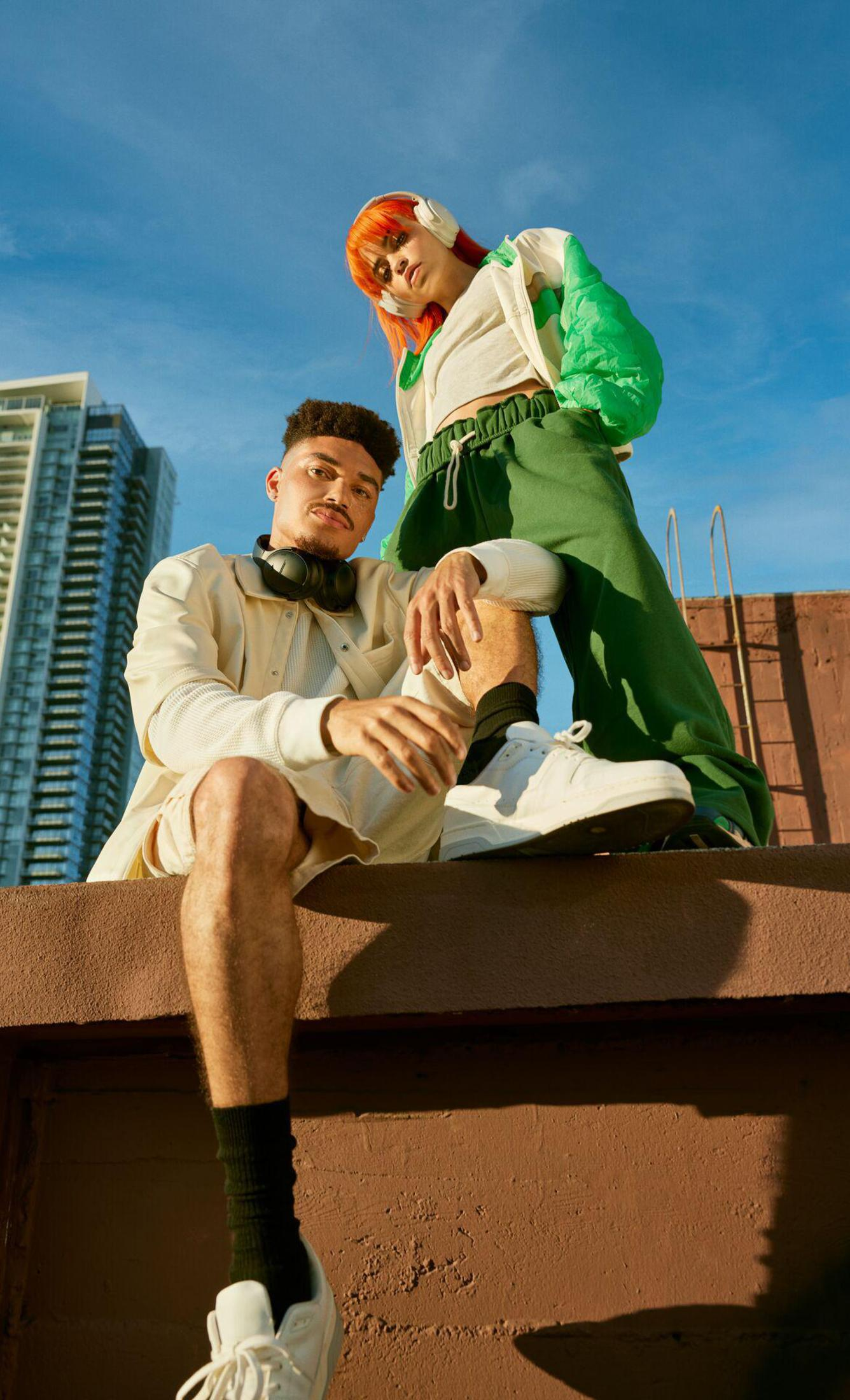 Dwie osoby na dachu, z drapaczami chmur w tle. Jedna siedzi, druga stoi.