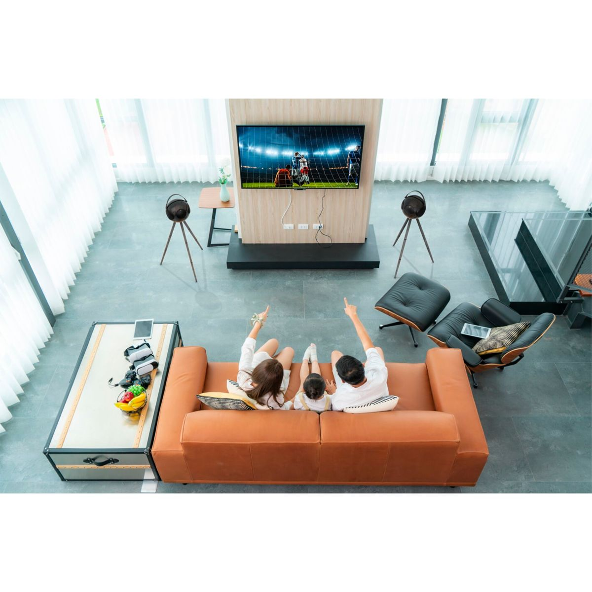 Rodzina oglądająca telewizję, dwa głośniki na stojakach, stolik kawowy ze sprzętem VR.