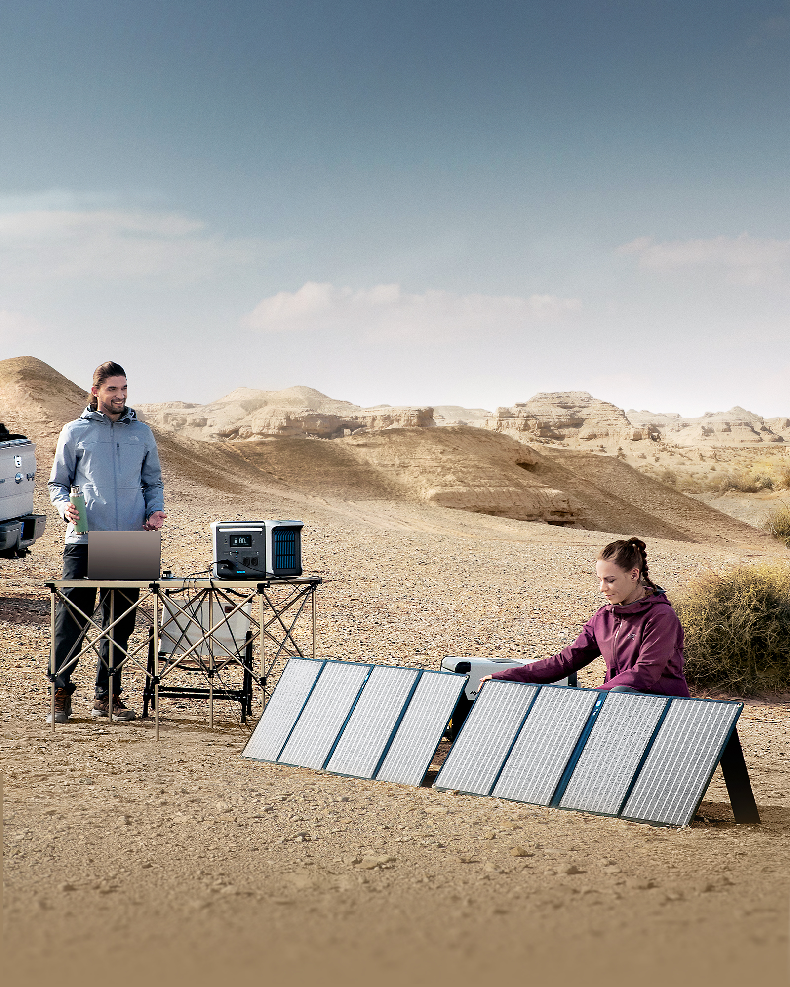 Zwei Personen mit Solarpanelen in einer Wüstenlandschaft, Laptop und Truck sind sichtbar.