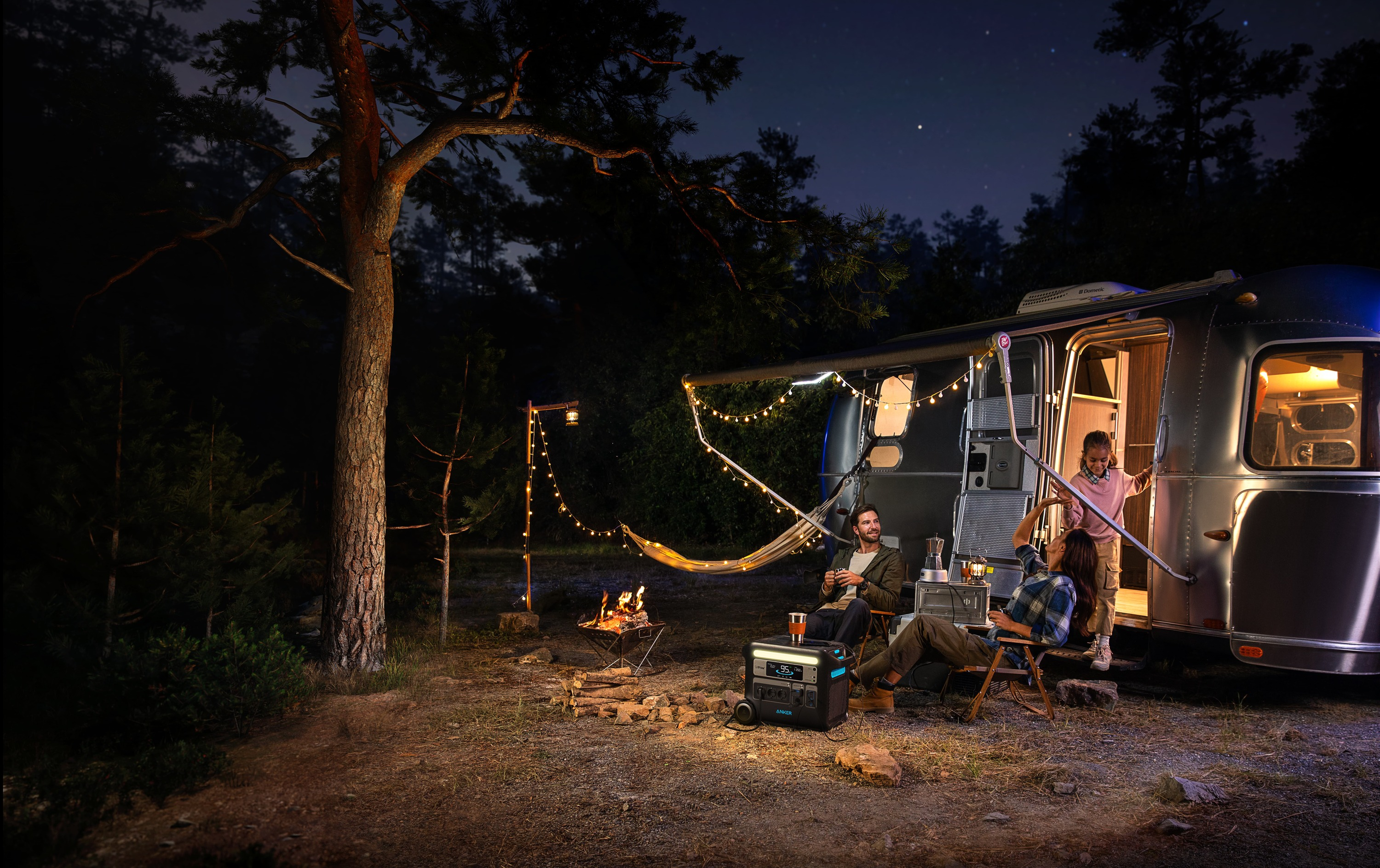 Scena nocnego kempingu. Ludzie wokół ogniska w pobliżu przyczepy kempingowej i drzew.