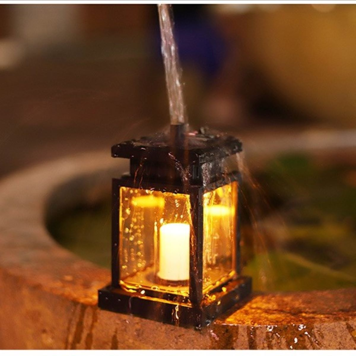 Schwarze Laterne mit Kerze, Wasser läuft darüber. Warmes Licht, verschwommener Hintergrund.