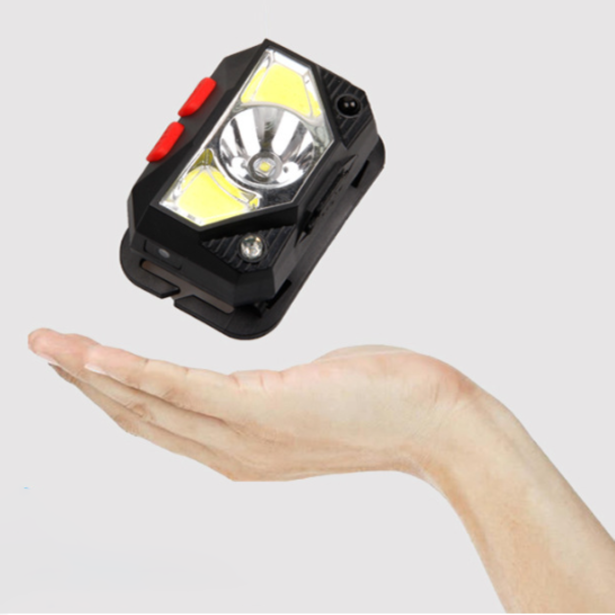 Schwarze LED-Stirnlampe wird in einer Hand gehalten. Stirnlampe hat rote Knöpfe und helles Licht.
