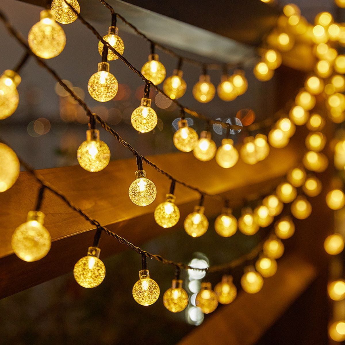 Lichterkette mit vielen kleinen, runden, durchsichtigen Glühbirnen, warmgelb beleuchtet, hängen von einer Holzkonstruktion.
