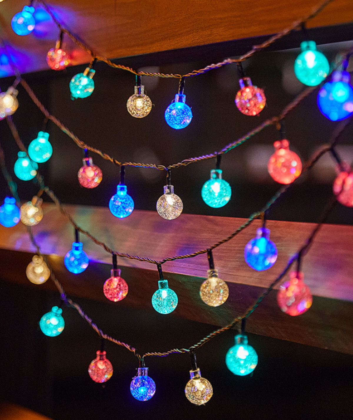 Lichterkette mit bunten Glühbirnen. Sie hängen vor Holzplanken.