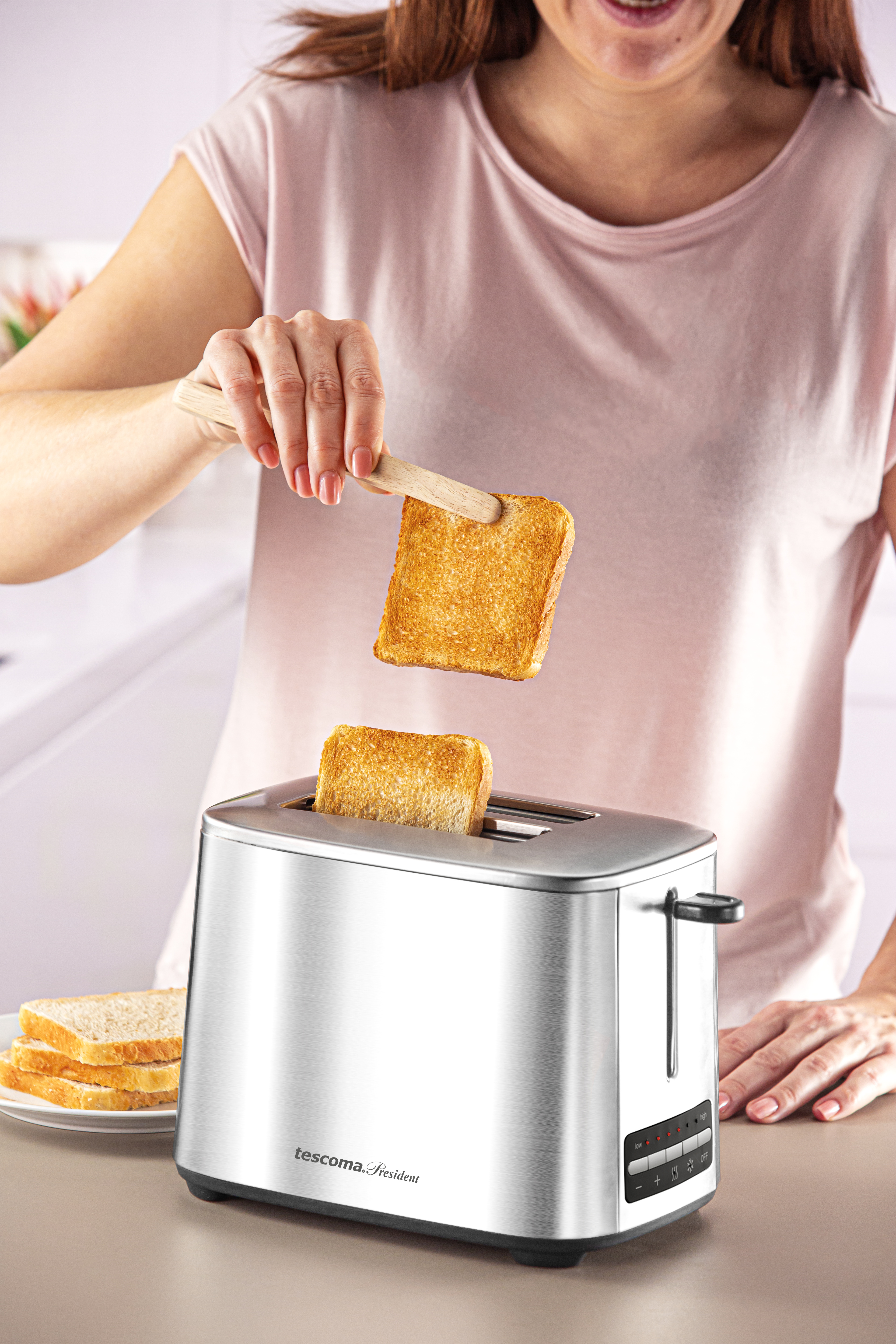 Eine Frau, die Toast mit einer Holzzange aus einem silbernen Toaster nimmt.