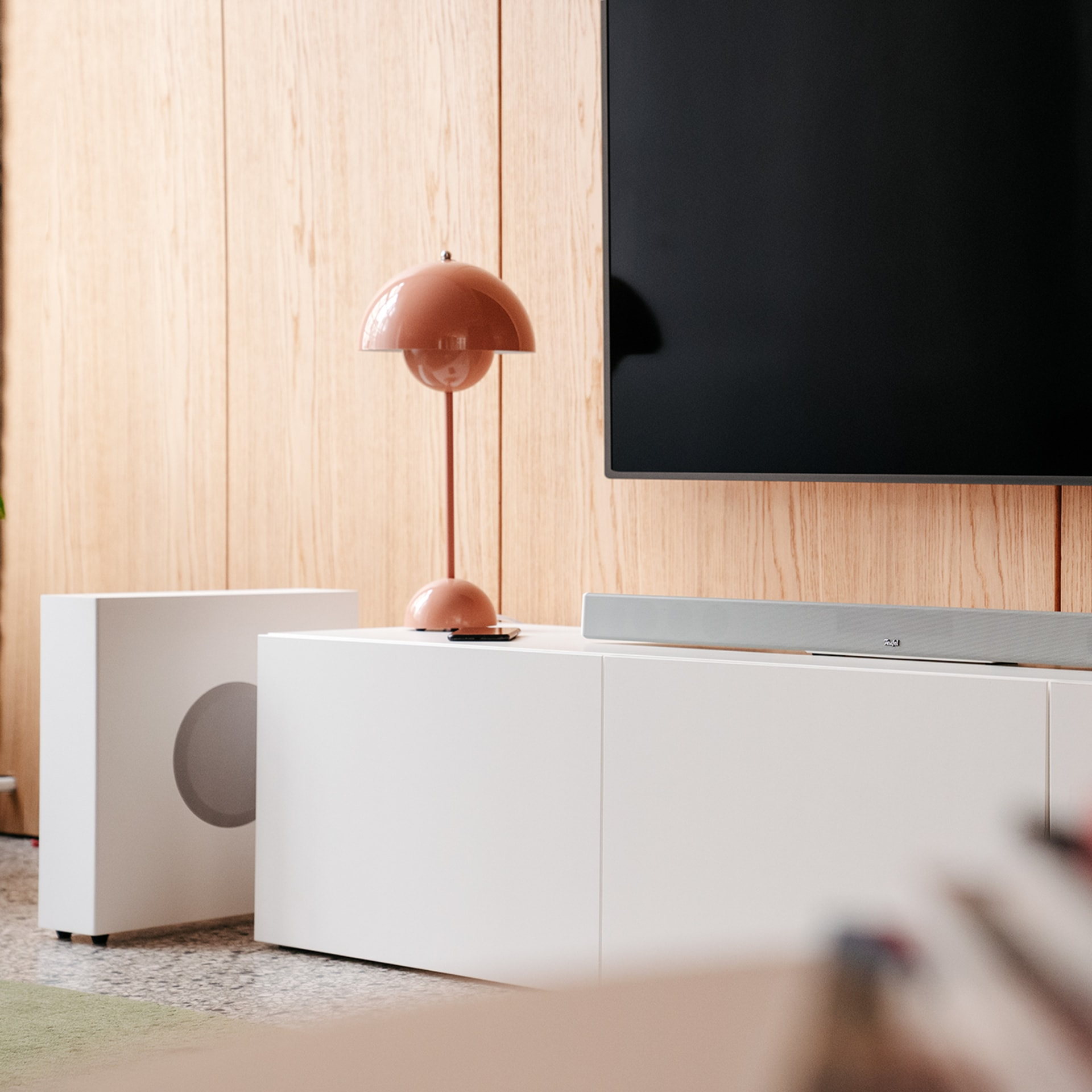 Innenszene mit einer Lampe, einem Subwoofer, einer Soundbar und einem Fernseher.