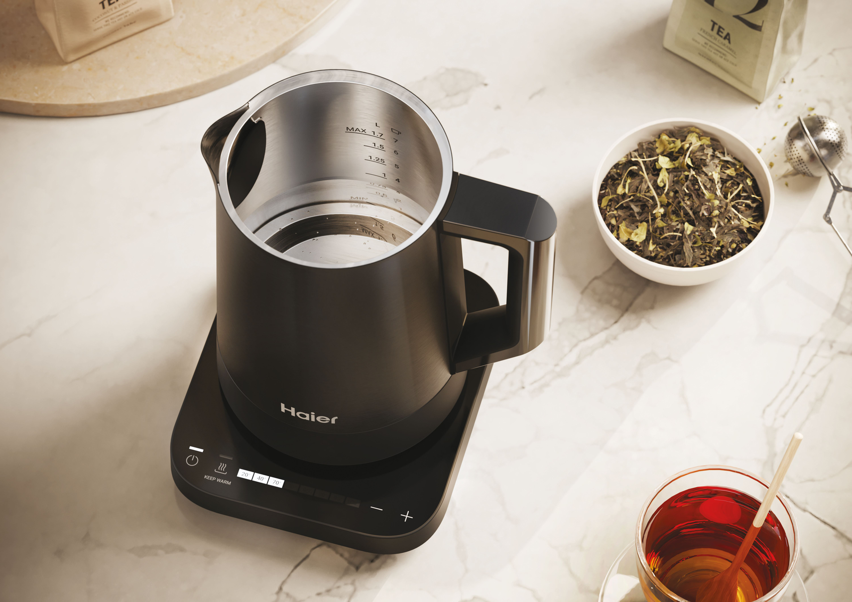 Czarny czajnik elektryczny na czarnej podstawie, ze wskaźnikami poziomu wody. Widoczna herbata i składniki.