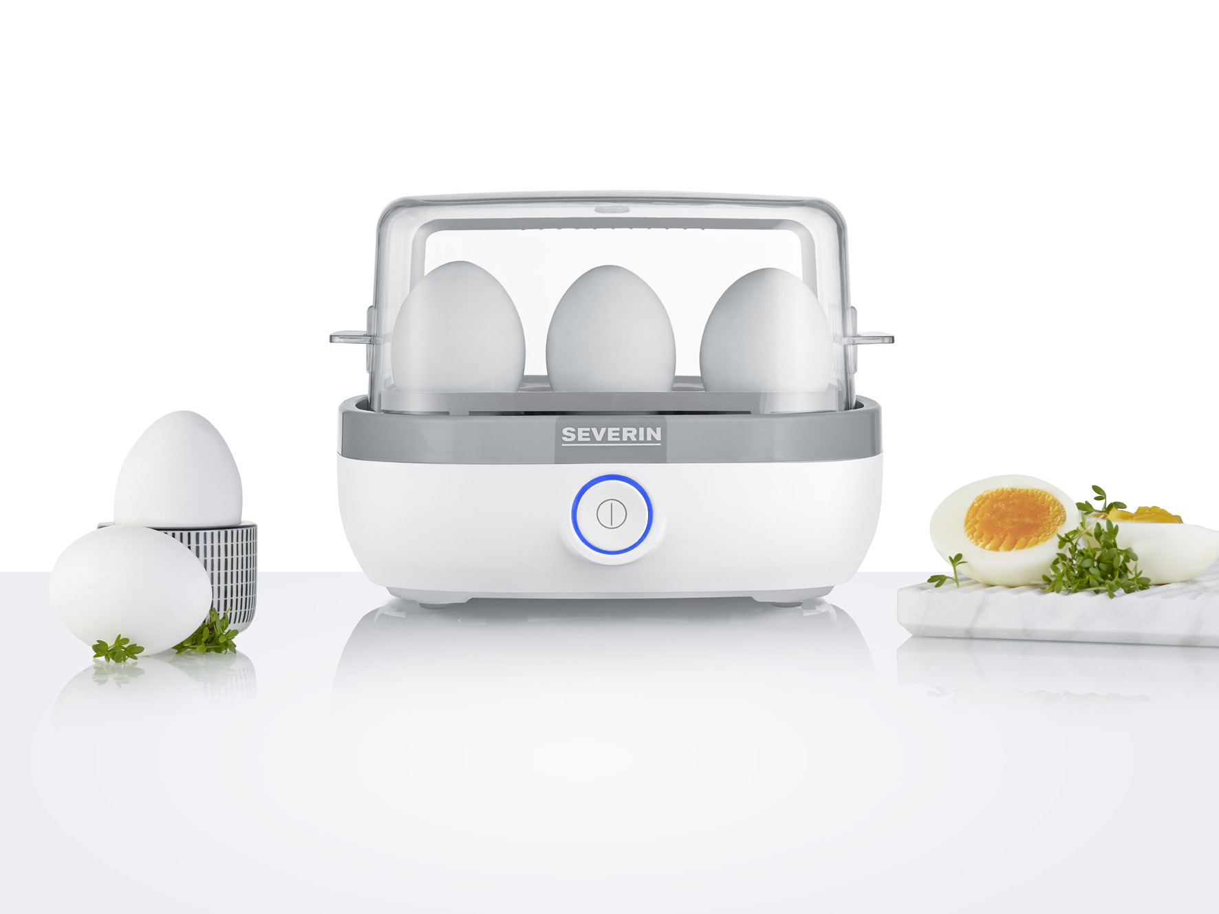 Gotowarka do jajek z trzema jajkami w środku, dwoma jajkami obok i przeciętym jajkiem.