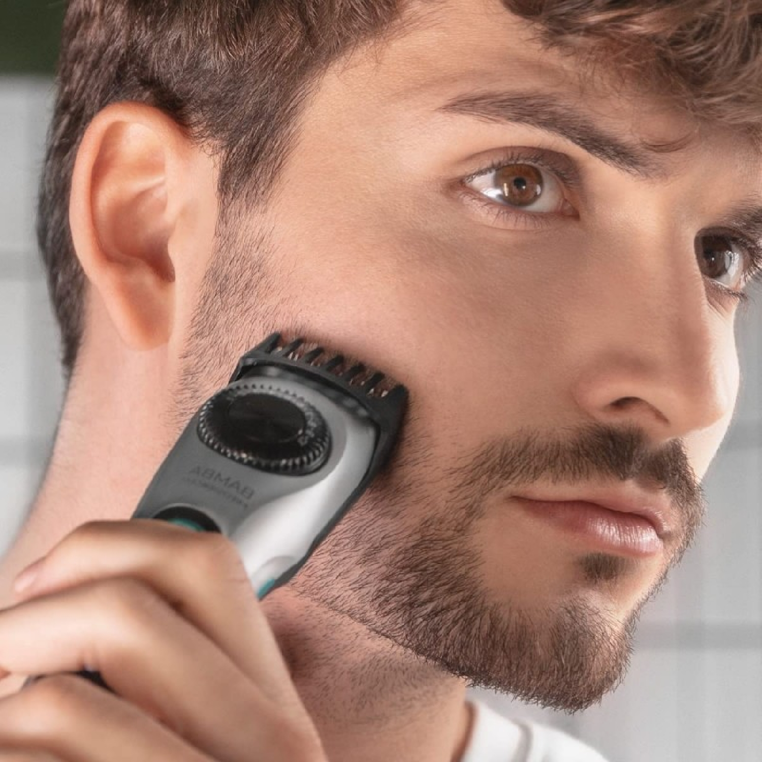 Man die een baardtrimmer gebruikt, close-up op zijn gezicht en het apparaat.