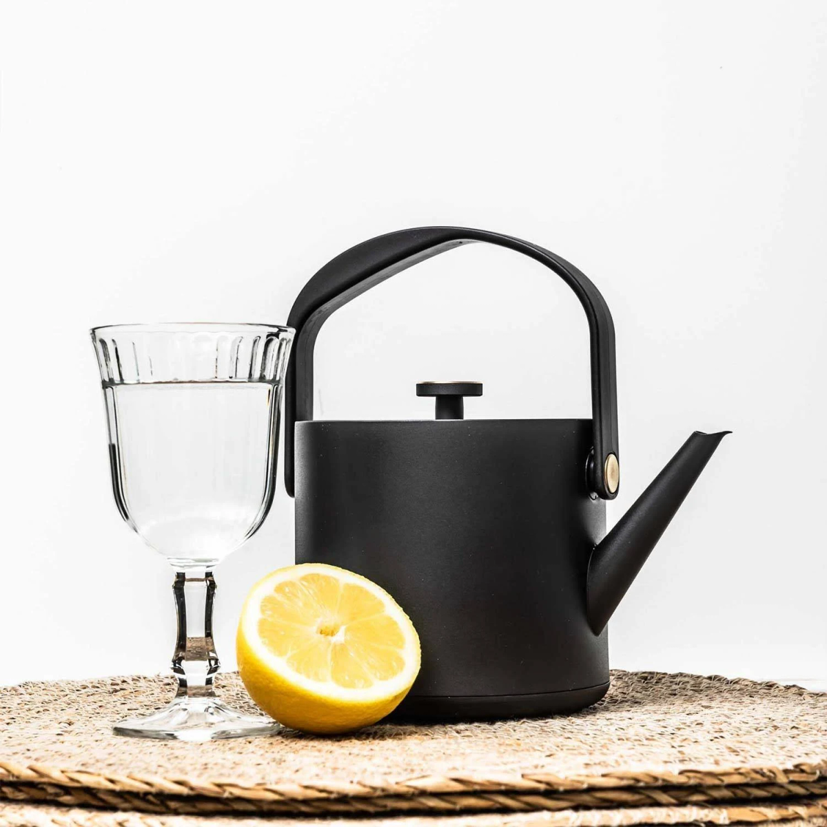 Una tetera negra junto a un vaso de agua y un limón.