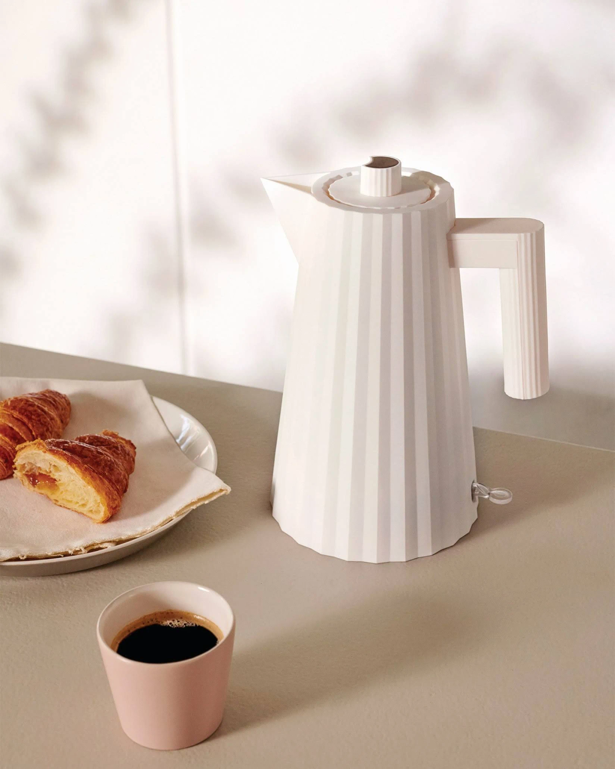 Bollitore elettrico bianco con una tazza di caffè e croissant.