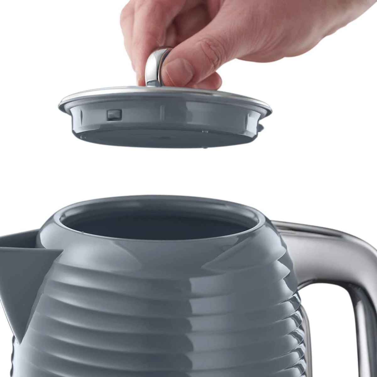 Una mano solleva il coperchio grigio da un bollitore elettrico grigio e cromato.