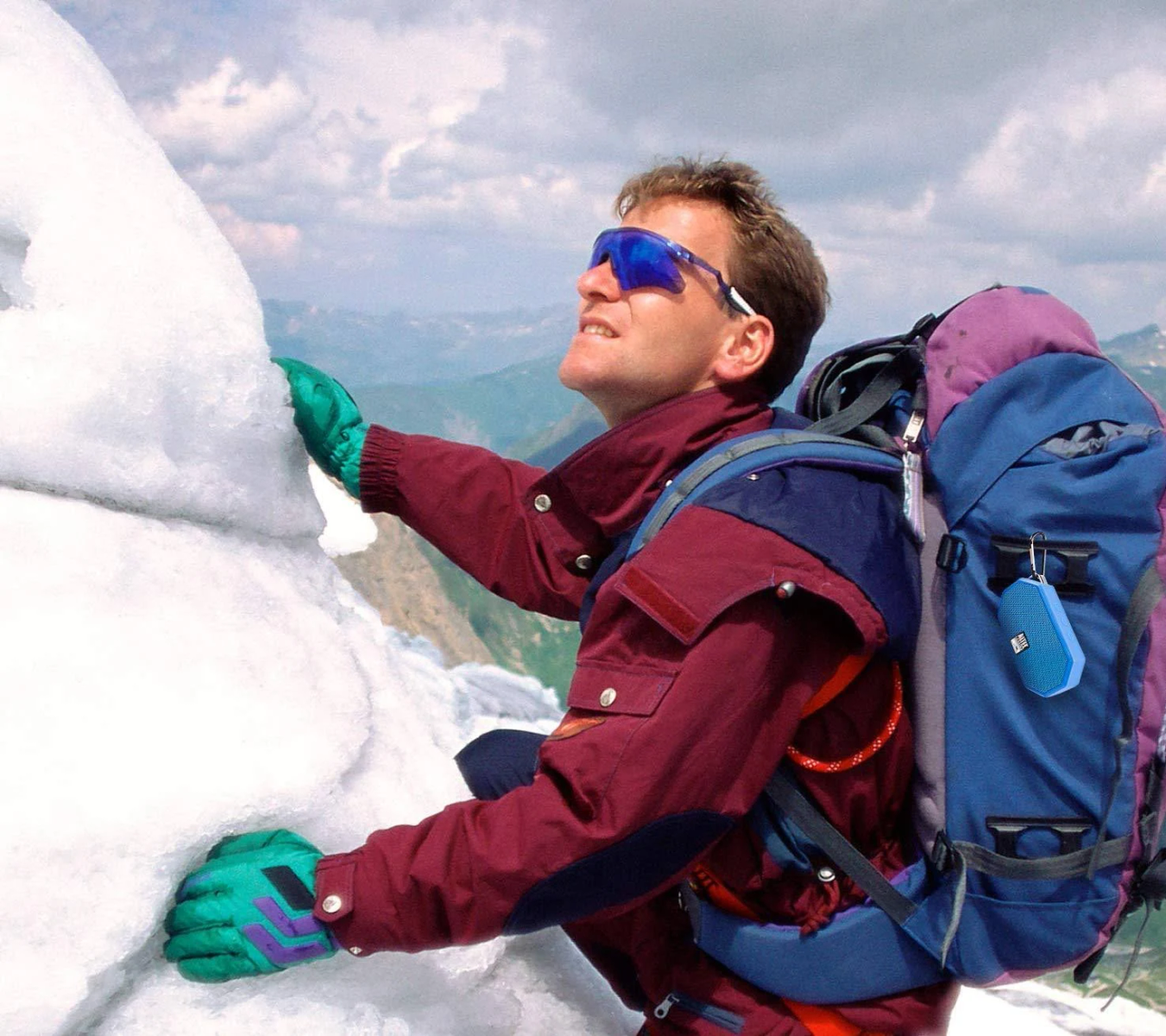 Un uomo che scala una montagna innevata, con occhiali da sole e uno zaino.