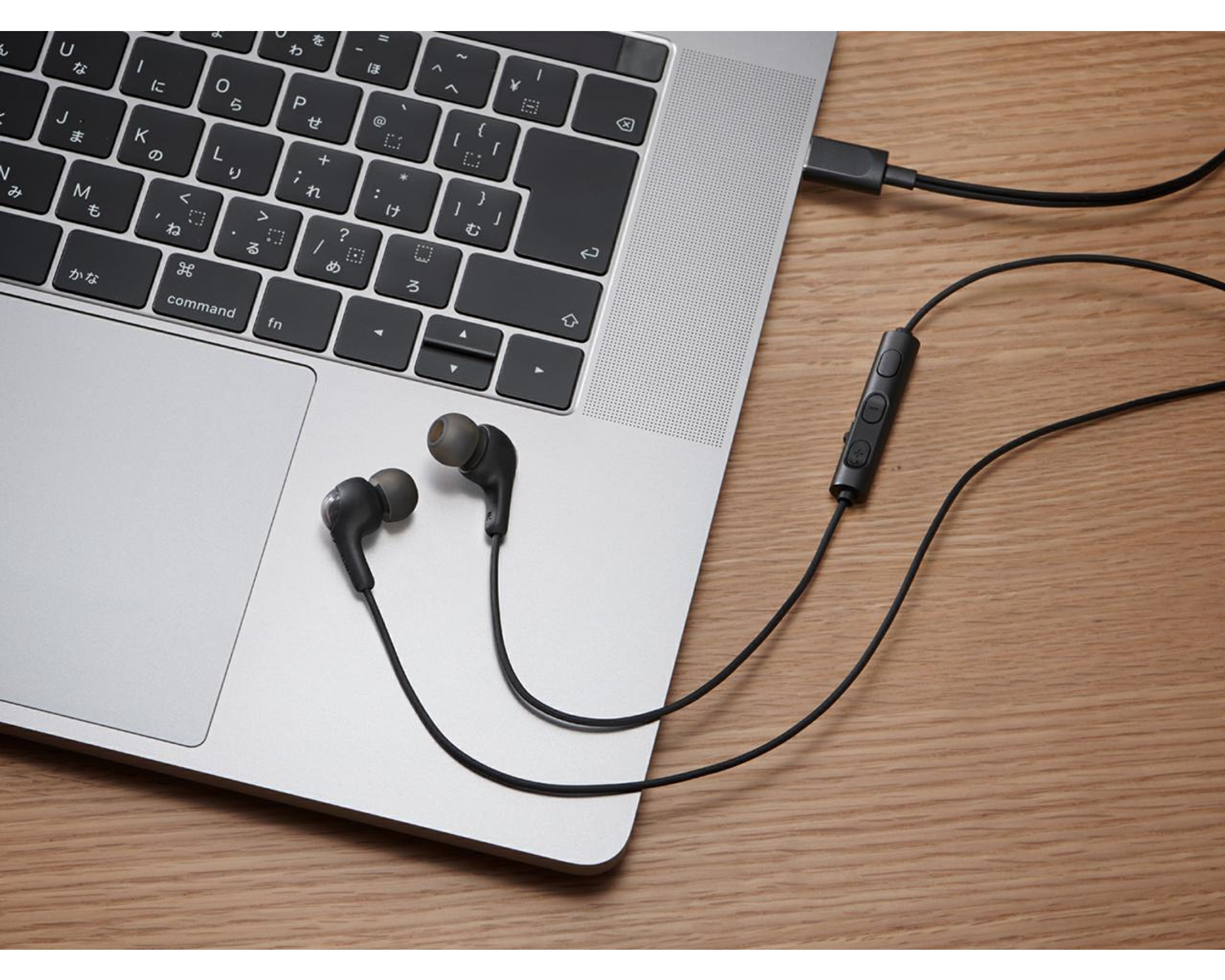 Czarne słuchawki podłączone do laptopa za pomocą kabla. Laptop znajduje się na drewnianej powierzchni.