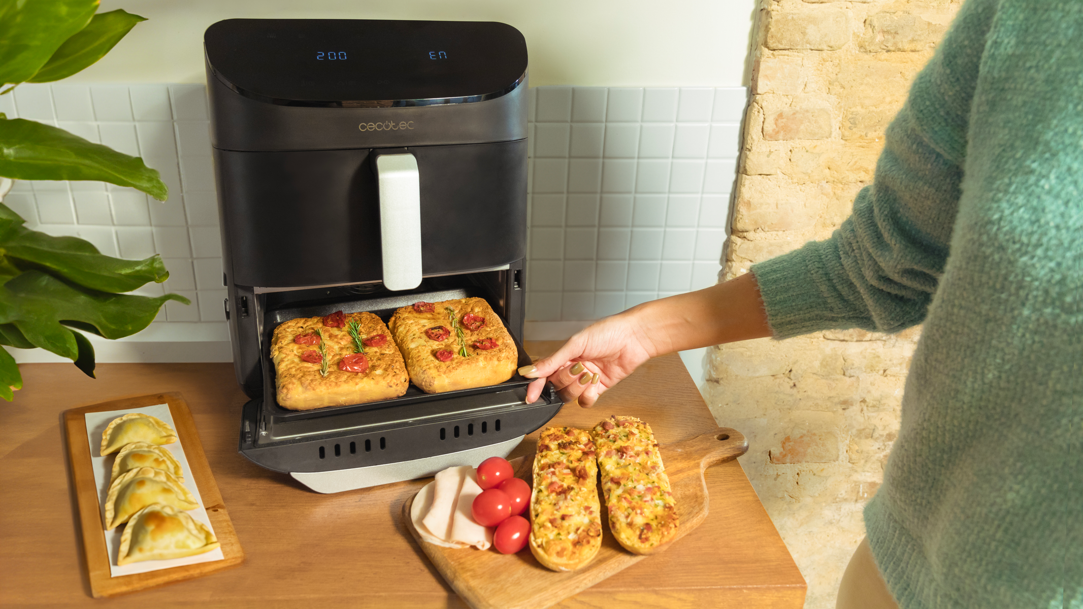Een persoon die een airfryer gebruikt. Gebakken focaccia en tomaten op tafel.