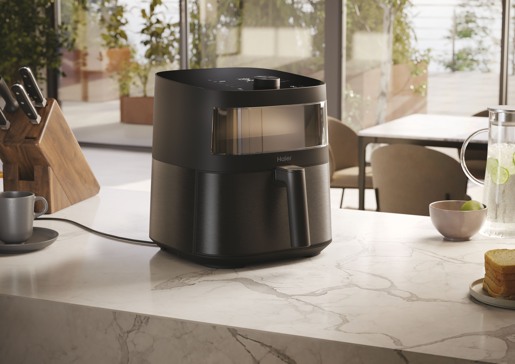 Czarna frytownica na blacie, obok dzbanka i chleba.