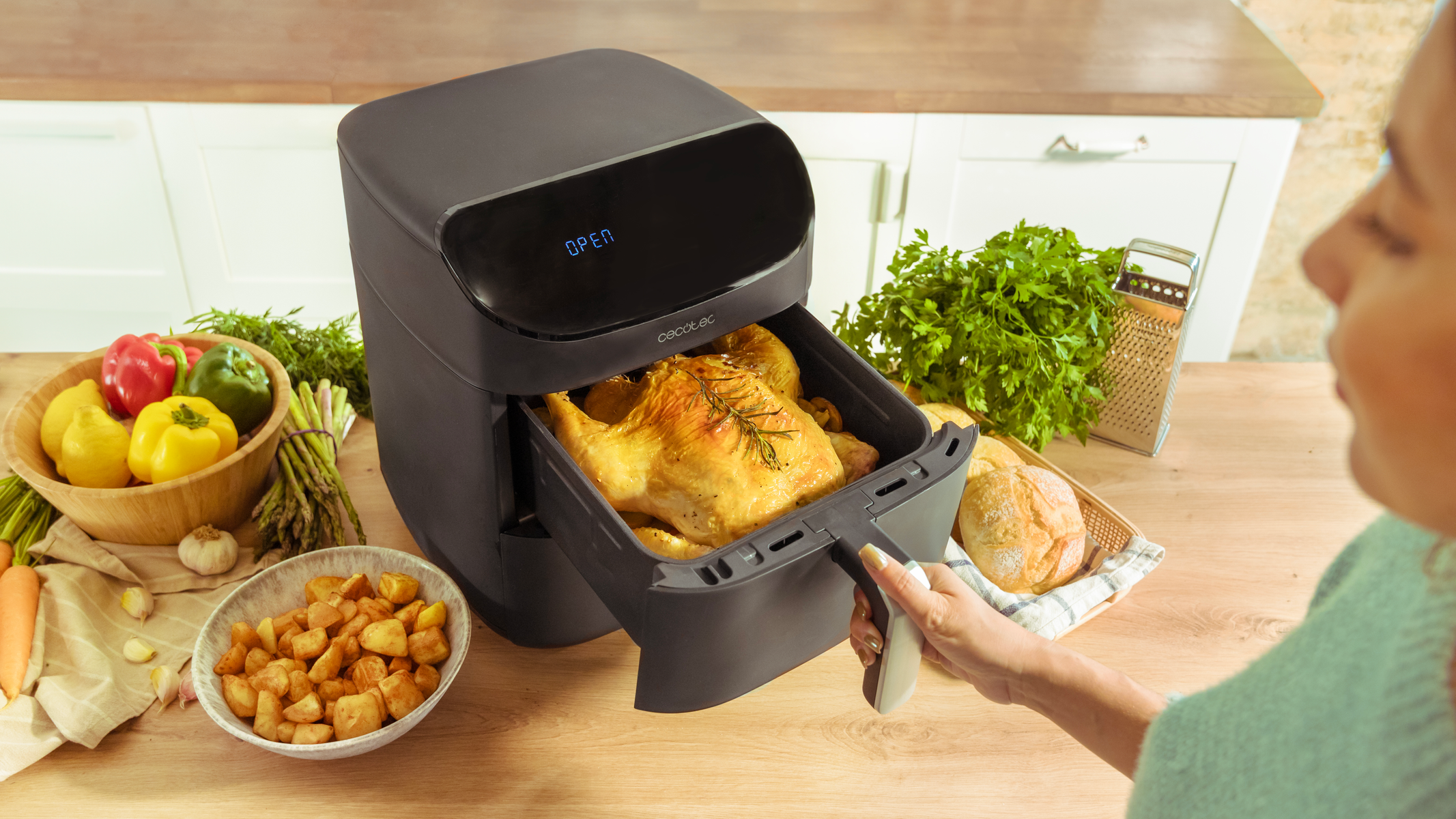Airfryer met kip. Vrouw opent de fryer. Groenten en aardappelen op tafel.