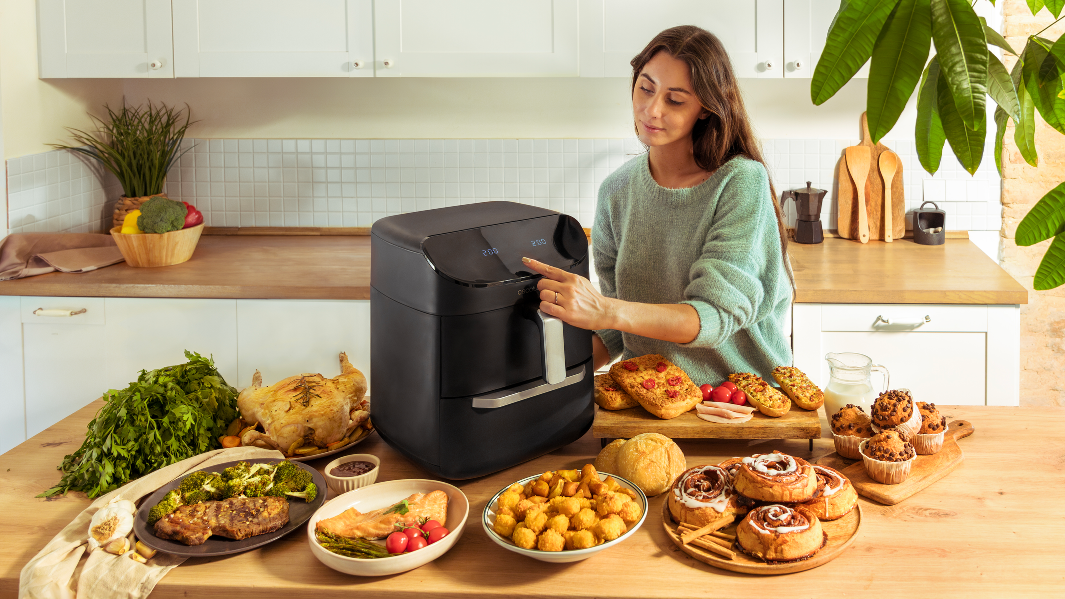 Een vrouw raakt een zwarte airfryer aan, omringd door verschillende voedingsmiddelen op een houten tafel.