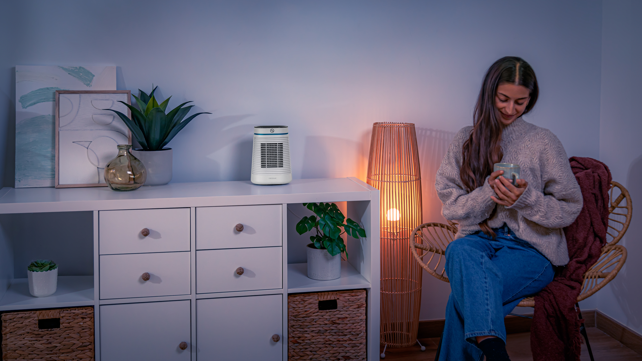 Donna seduta, tiene una tazza, vicino a un termosifone e una lampada da terra. Stanza accogliente.