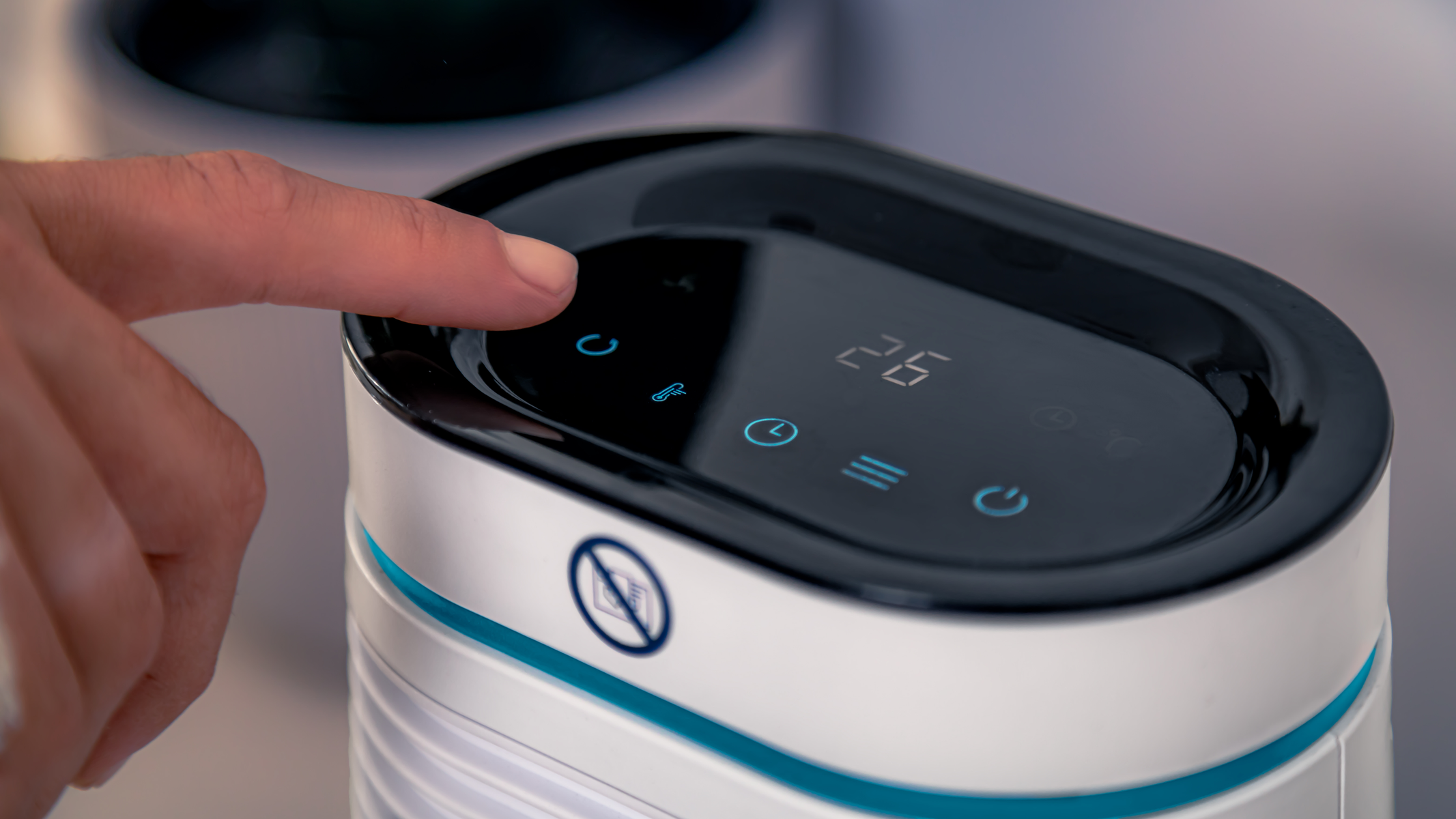 Un dito preme un pulsante su un dispositivo bianco e verde acqua che mostra la temperatura digitale.