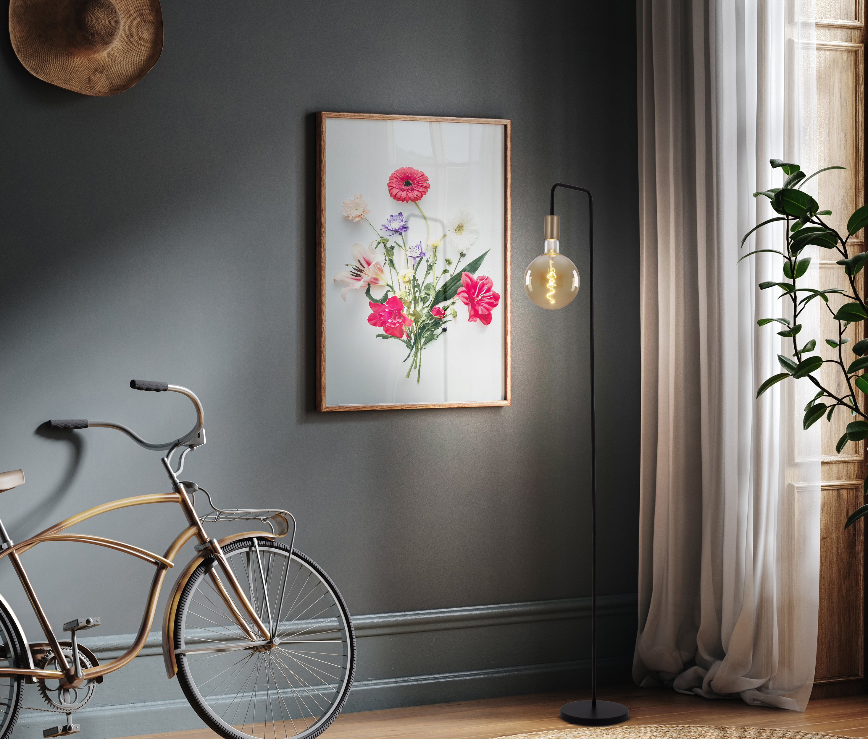 Ein Raum mit Fahrrad, Kunstdruck und Stehlampe. Die Wand ist grau, der Boden Holz. Natürliches Licht.