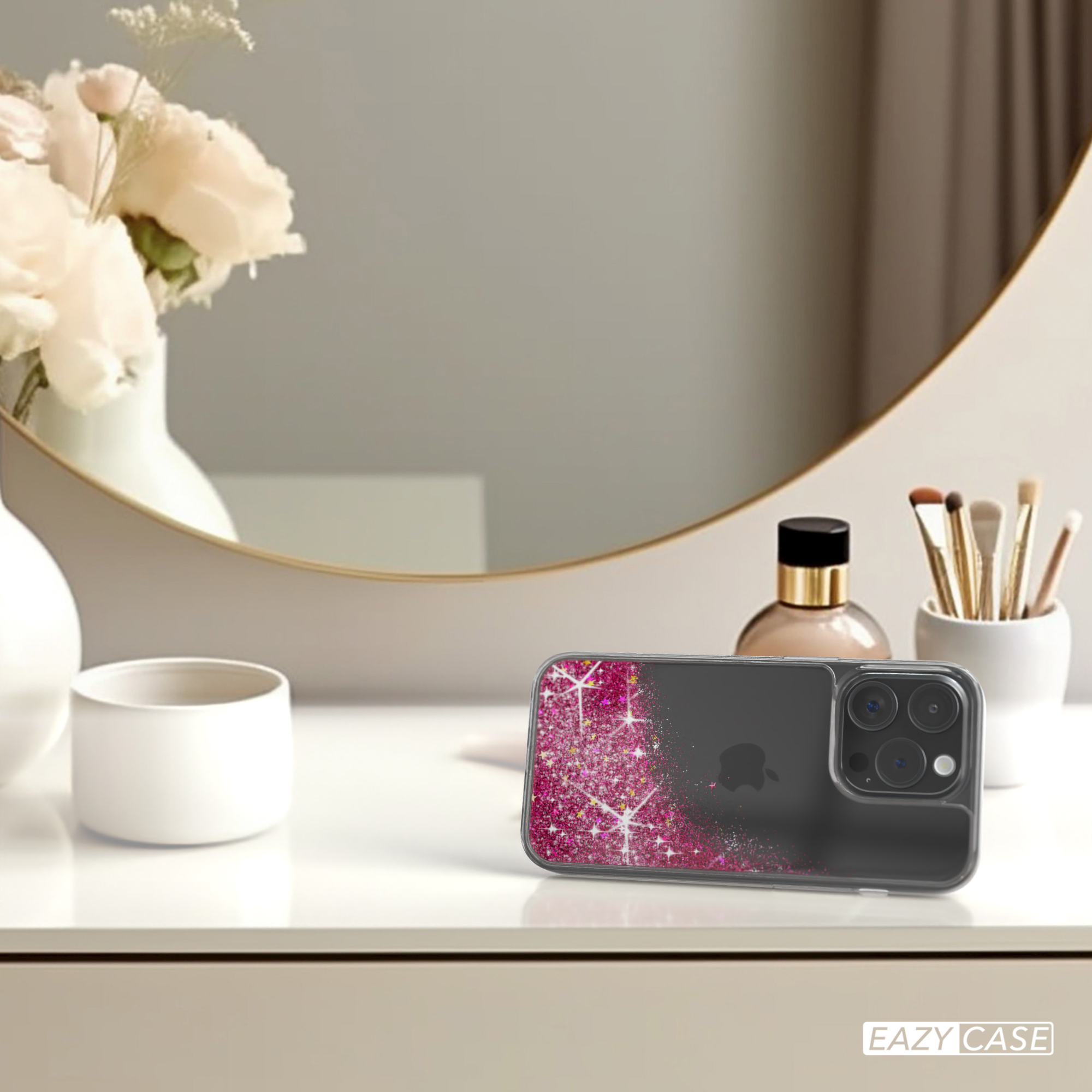 iPhone-Hülle mit rosa Glitzer-Design, liegt auf einem Tisch mit Spiegel und Blumen im Hintergrund.