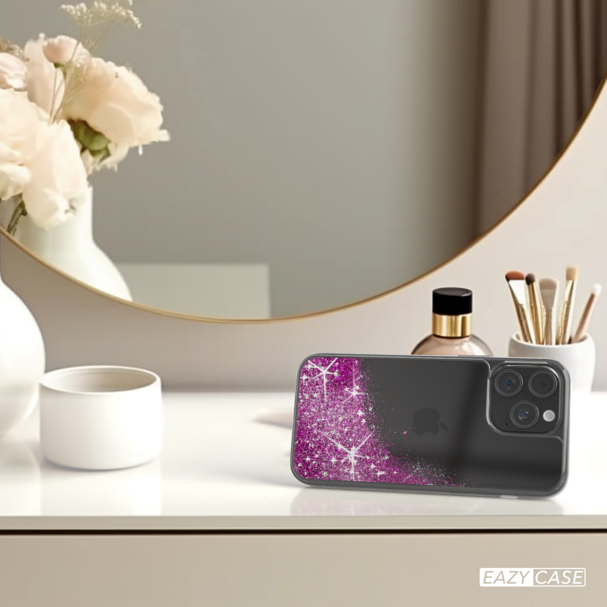 Telefon mit pinkfarbener Glitzerhülle auf einem Tisch, mit Blumen und Make-up-Zubehör.