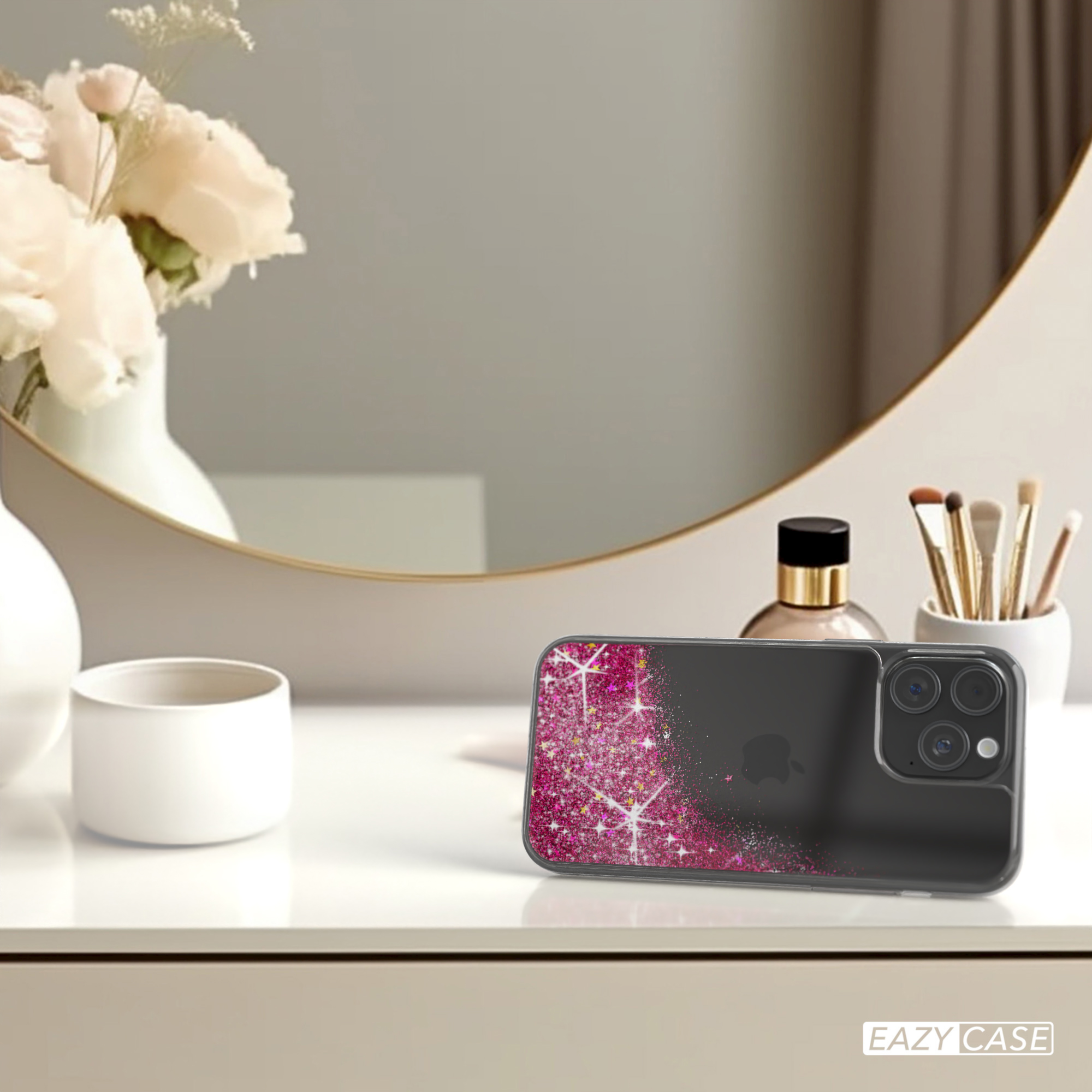 Ein Telefon in einer pinken Glitzerhülle auf einem weißen Schreibtisch. Im Hintergrund Spiegel, Blumen und Kosmetik.