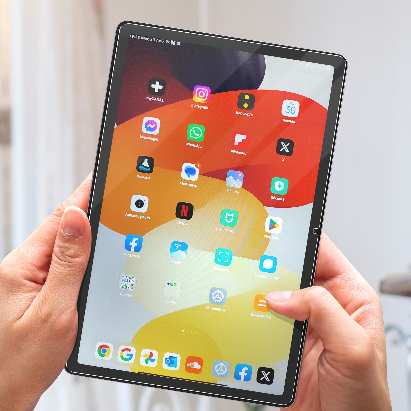 Un tablet è tenuto con due mani, lo schermo mostra app. Lo sfondo è un'ambientazione domestica.