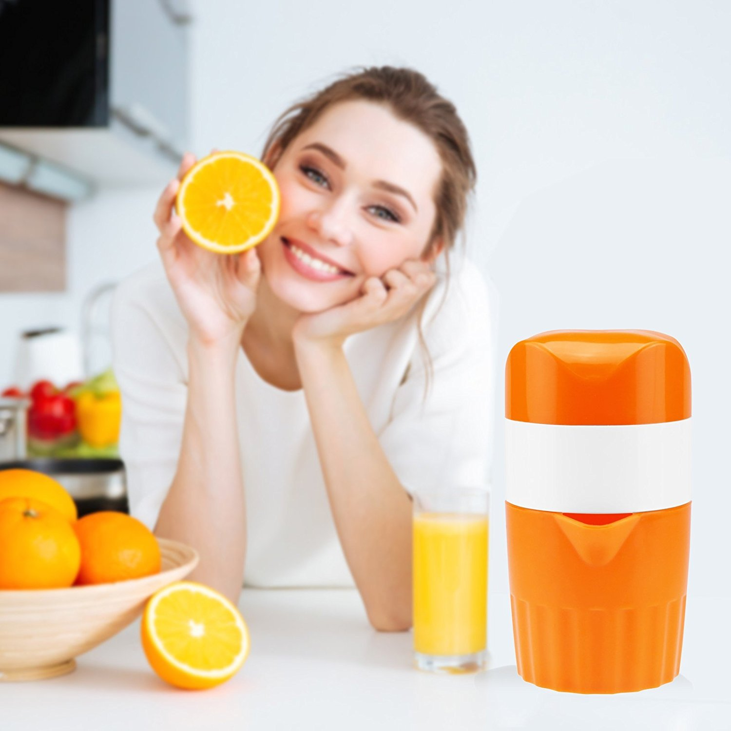 Frau hält eine Orangenhälfte, neben einer Saftpresse und einer Schüssel Orangen. Lächelt.