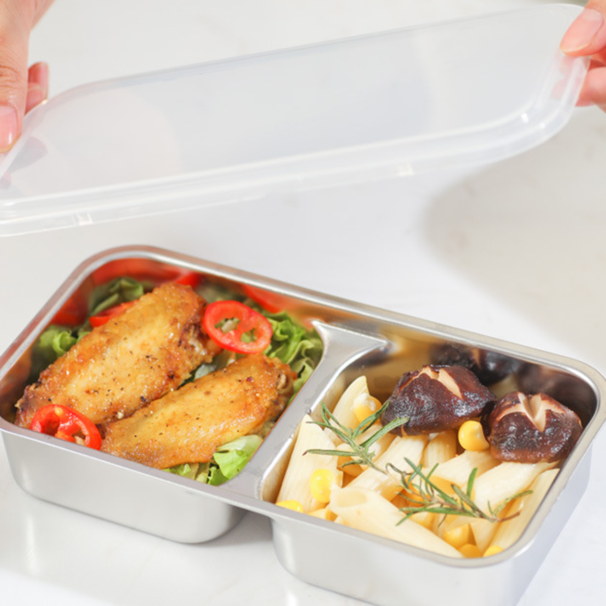 Lunchbox mit Flügeln, Tomaten, Nudeln mit Mais, Pilzen und Rosmarin. Weißer Hintergrund.