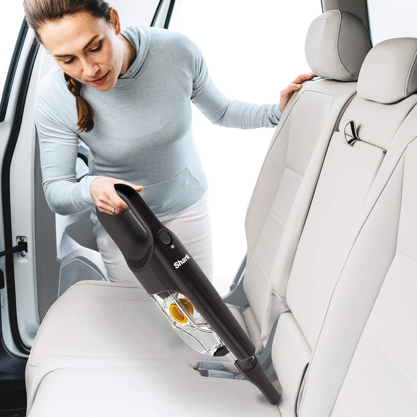 Eine Frau reinigt einen Autositz mit einem schwarzen Handstaubsauger.