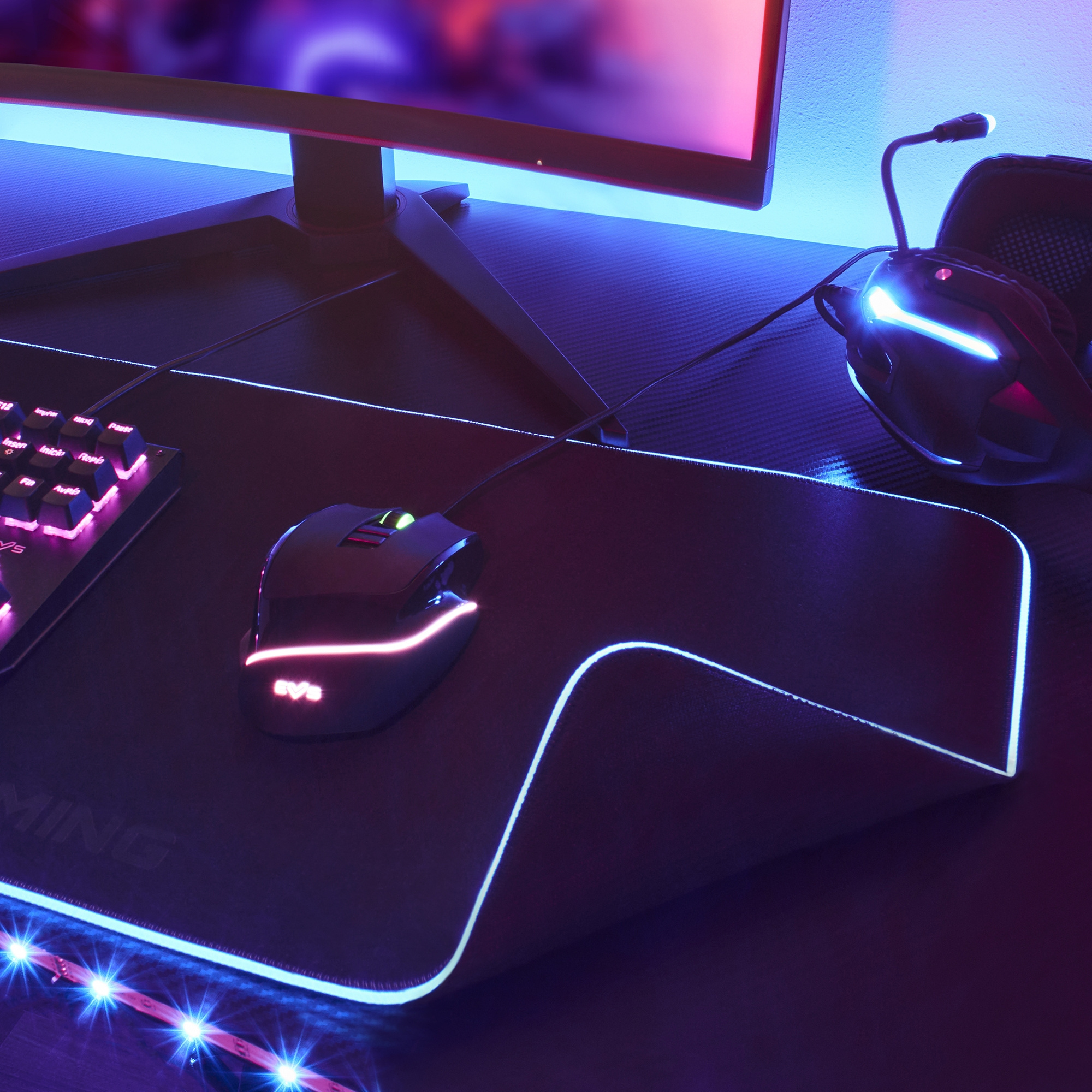 Configuración de juego con ratón en alfombrilla, teclado, monitor y auriculares. Luz azul.