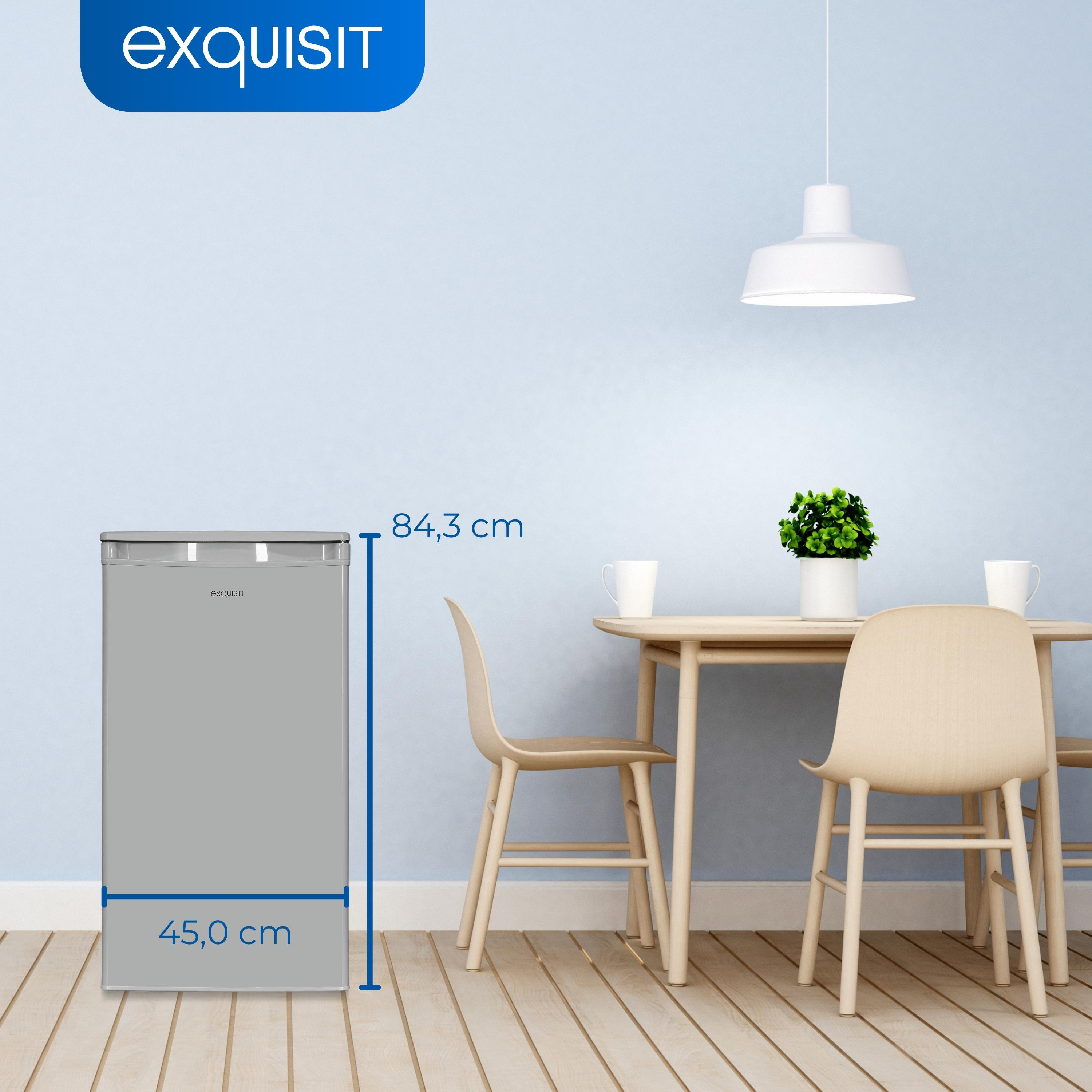 Grauer Kühlschrank mit Maßen, vor einem Esstisch mit Stühlen und Lampe.